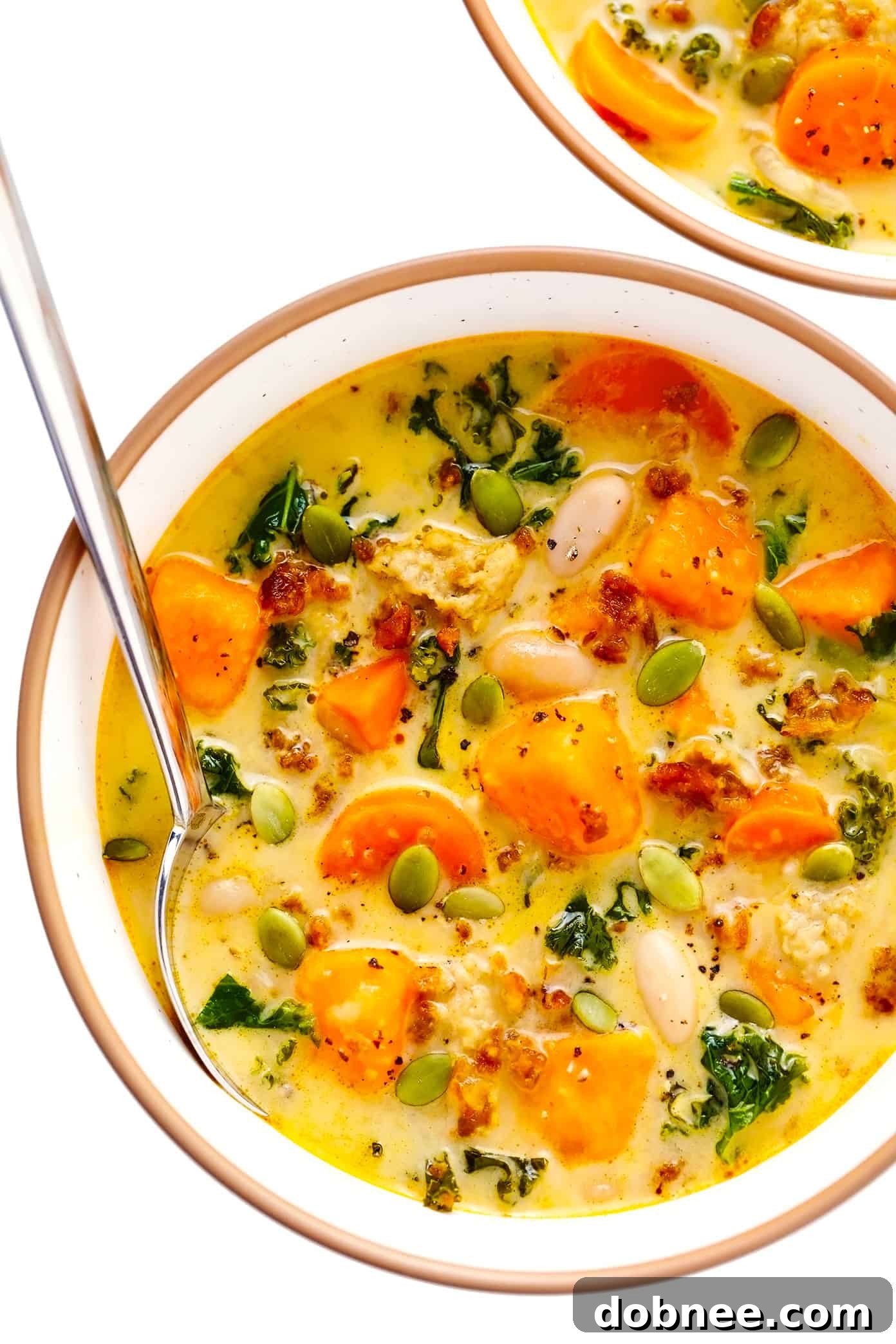 Serving bowl of creamy sweet potato and sausage soup with white beans and kale, ready to enjoy.
