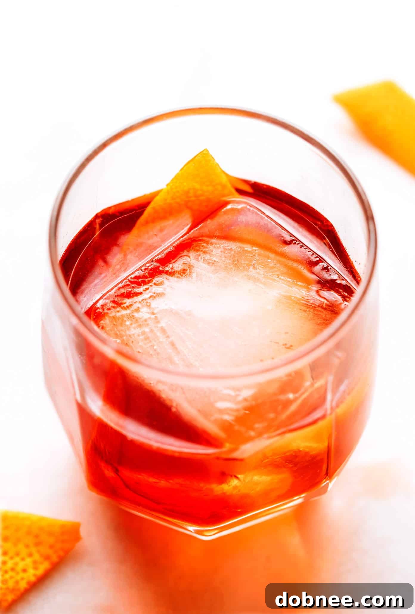 A stunning Boulevardier cocktail, garnished with a vibrant orange twist, served in a classic rocks glass with a large ice cube.