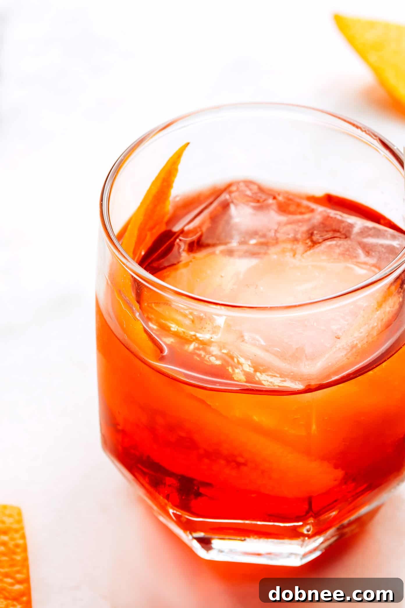 A perfectly prepared Boulevardier cocktail in a rocks glass, featuring a large, clear ice cube and a twisted orange peel garnish, ready for enjoyment.
