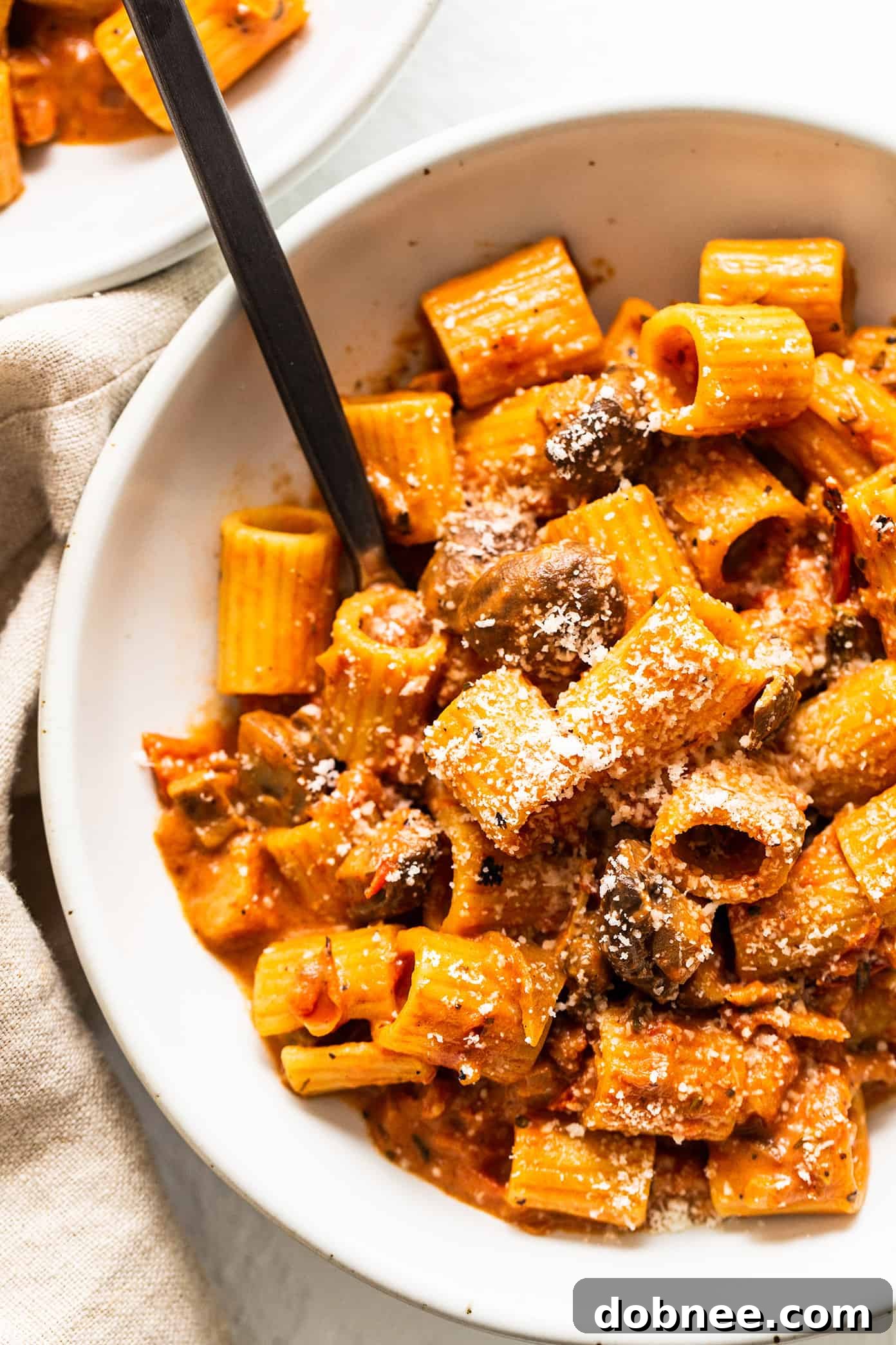 A bowl of creamy Pasta alla Boscaiola topped with freshly grated Parmesan cheese