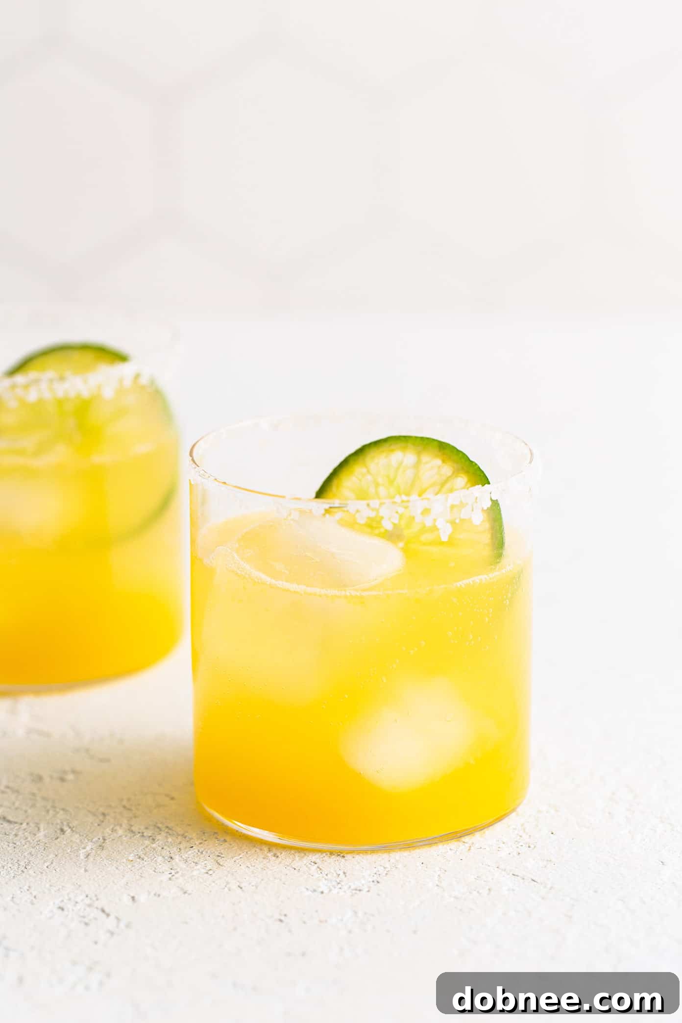 Two Virgin Margarita Mocktails in glasses, garnished with lime slices, showcasing their vibrant color and refreshing appeal.