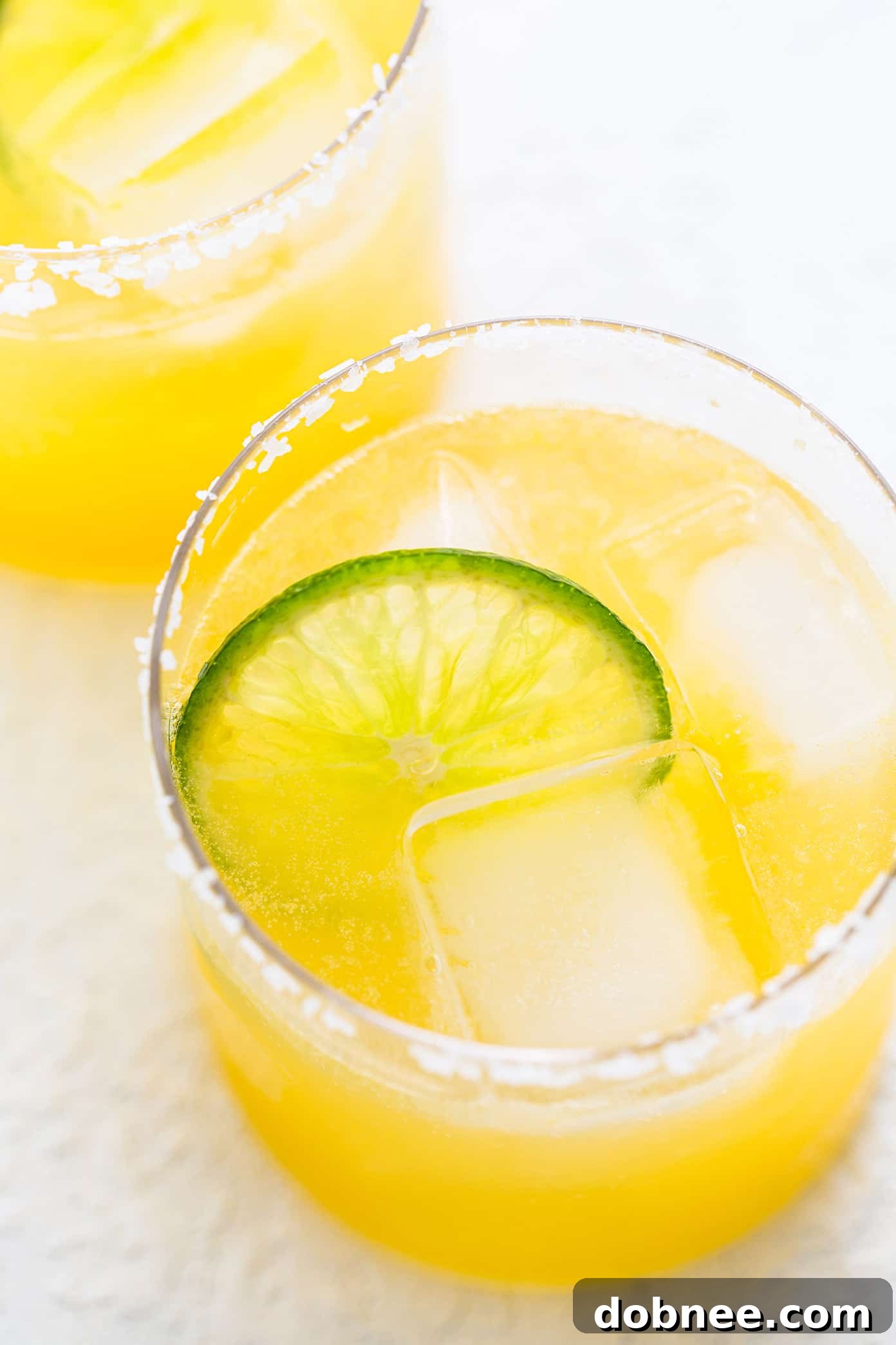 Four Virgin Margarita Mocktails in glasses with salt rims and lime garnishes, ready to be served and enjoyed at a gathering.