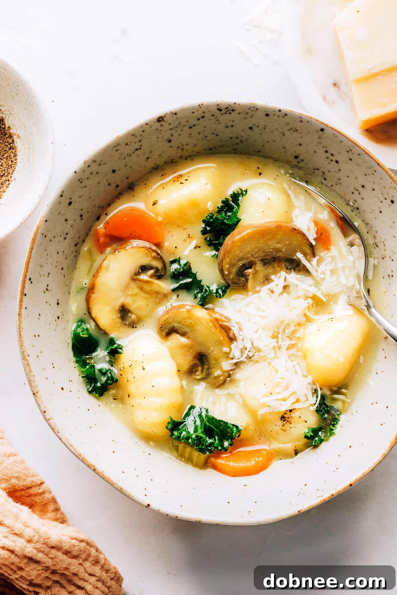 Hearty and comforting Gnocchi, Mushroom and Kale Soup with a creamy garlic-rosemary broth, garnished with fresh Parmesan cheese.