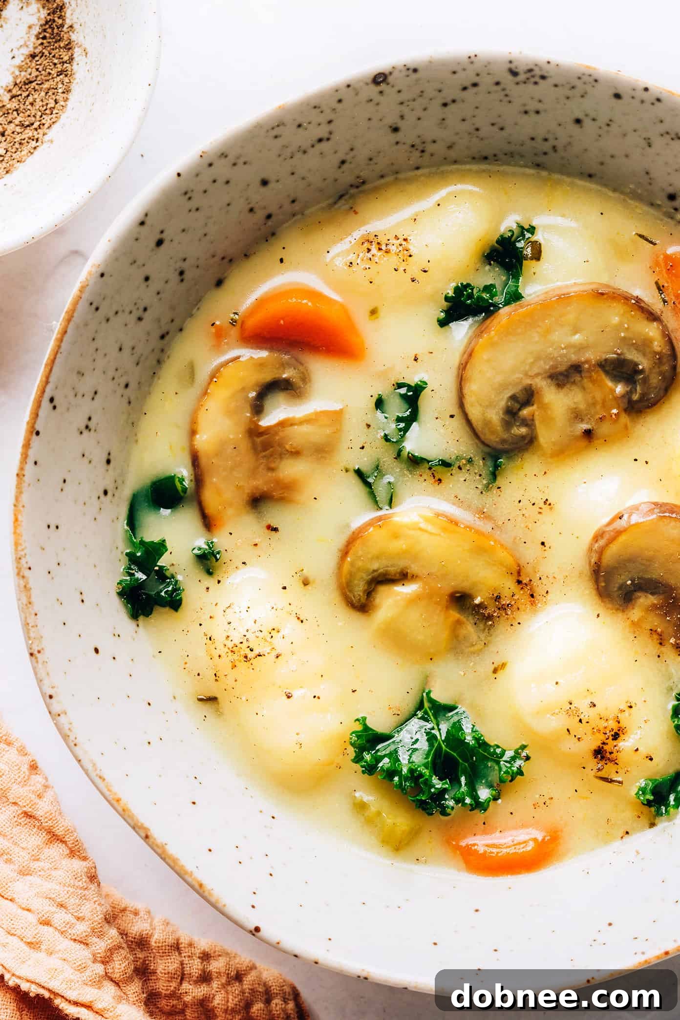 A close-up of a serving of creamy Gnocchi, Mushroom, and Kale Soup, garnished with fresh Parmesan and herbs.