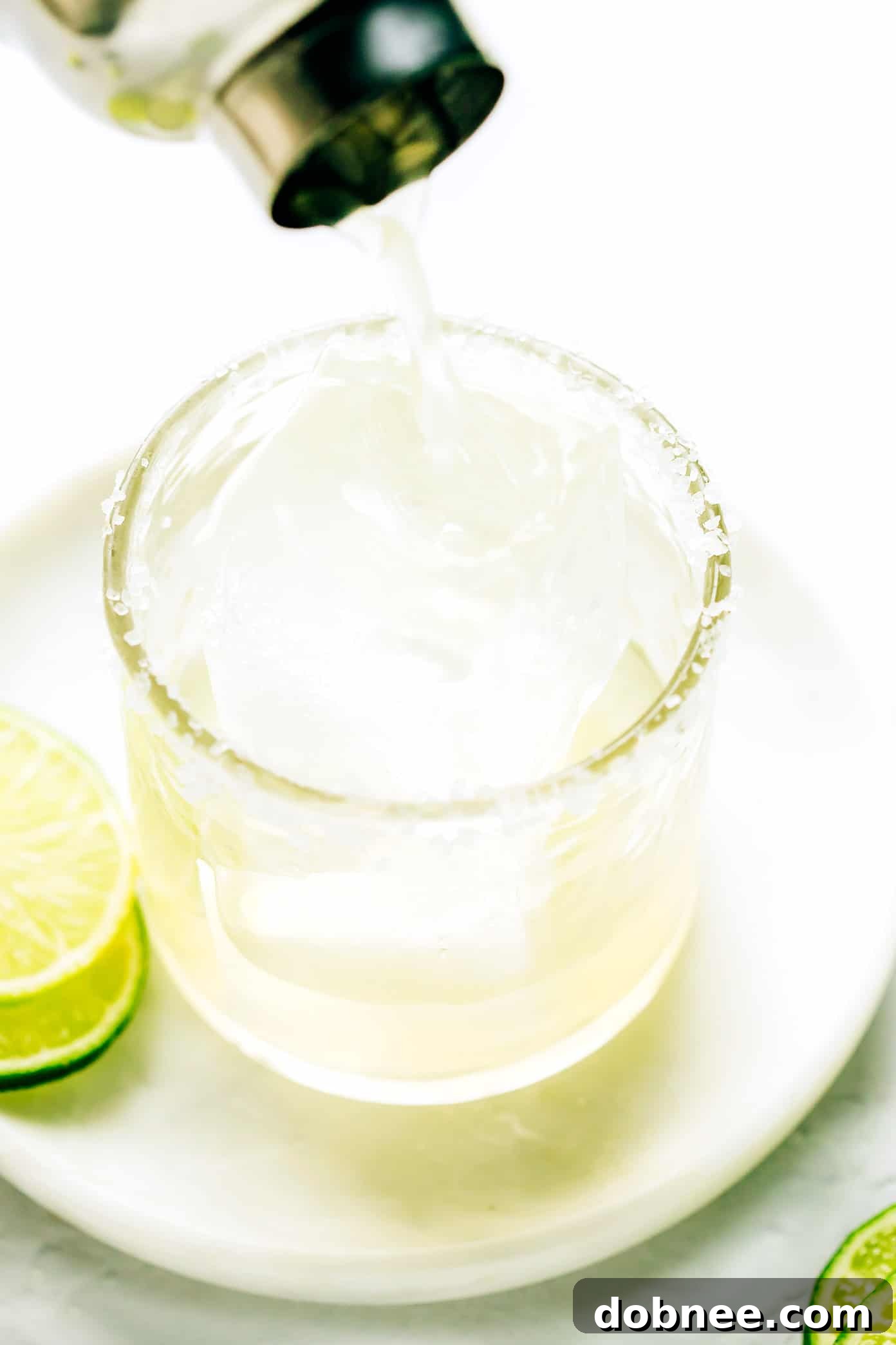 Pouring a freshly shaken Bourbon Margarita into a salt-rimmed glass filled with ice, ready for garnish.