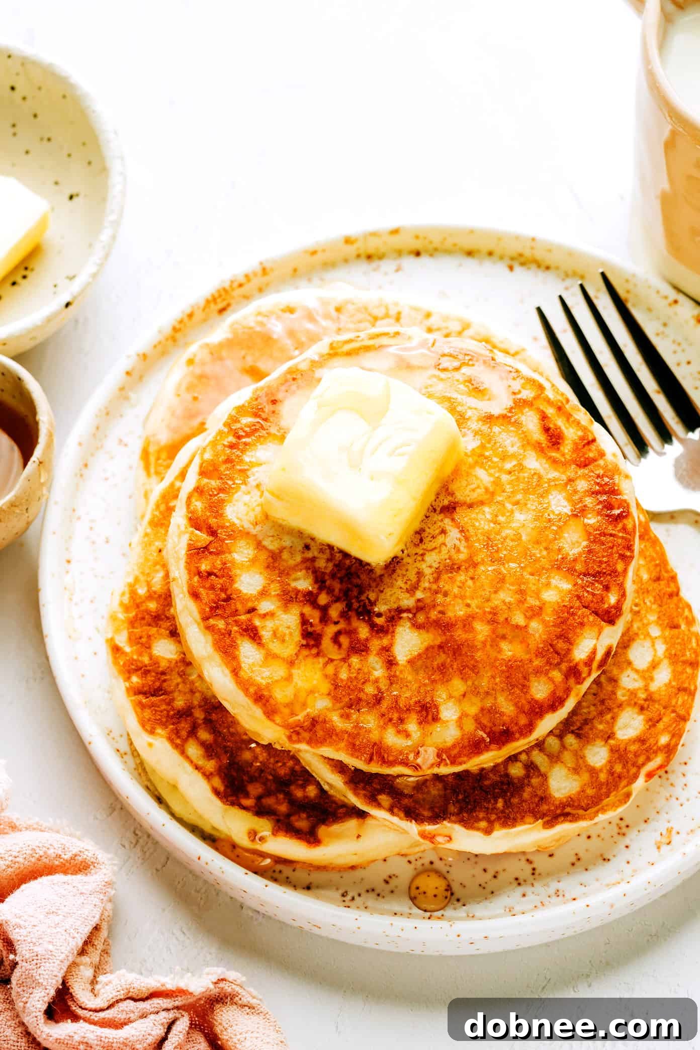Stack of golden brown fluffy kefir pancakes drizzled with maple syrup and topped with fresh berries