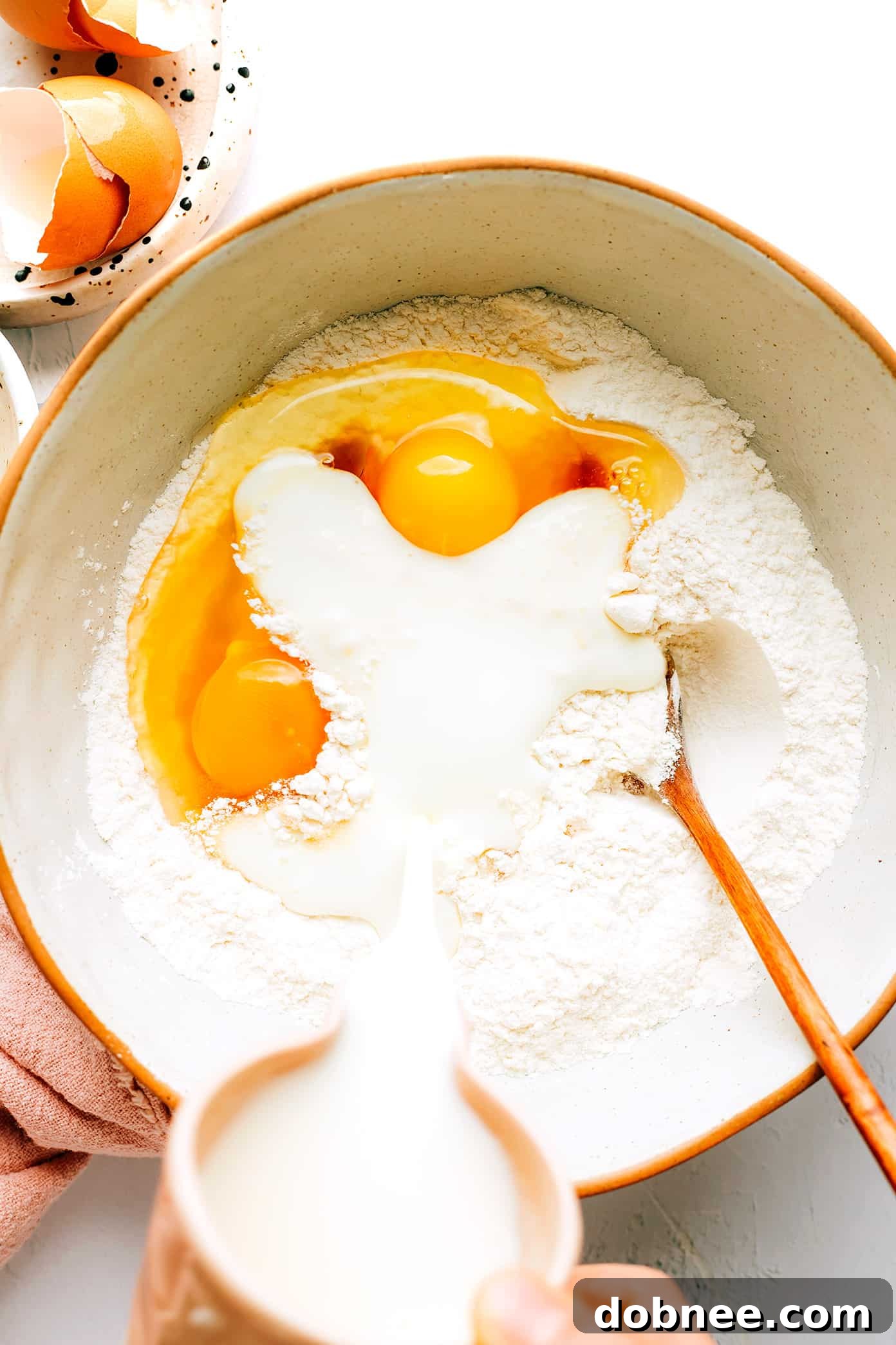 A mixing bowl filled with kefir pancake batter, with measuring cups and ingredients nearby
