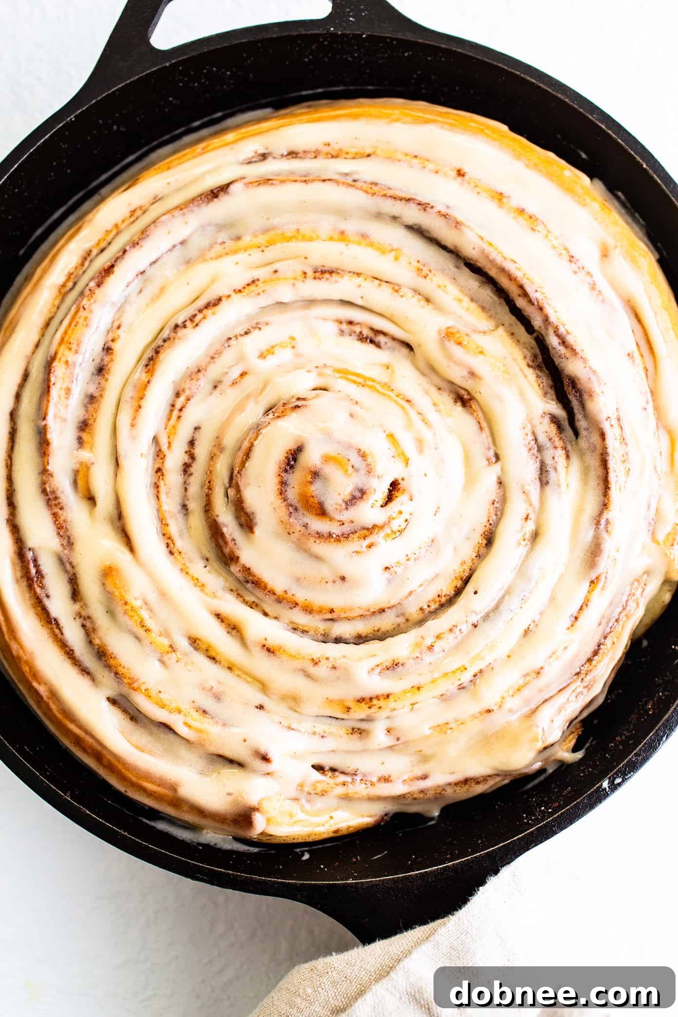 Finished Giant Cinnamon Roll with Cream Cheese Icing A glorious giant cinnamon roll baked in a cast iron skillet, completely covered with smooth, white cream cheese icing.