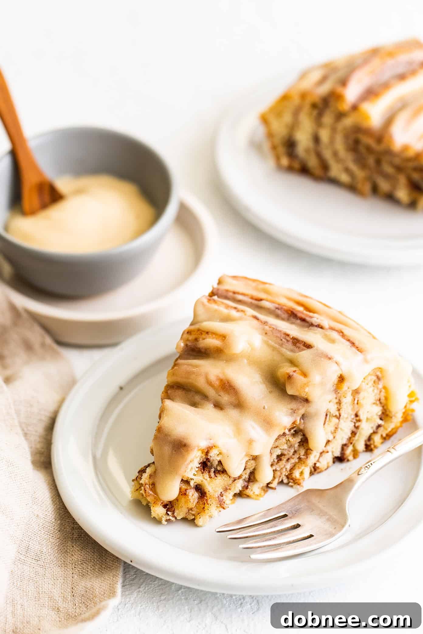 Serving Slices of Giant Cinnamon Roll Several generous slices of the giant cinnamon roll, each topped with a swirl of rich cream cheese frosting, on a white serving plate.