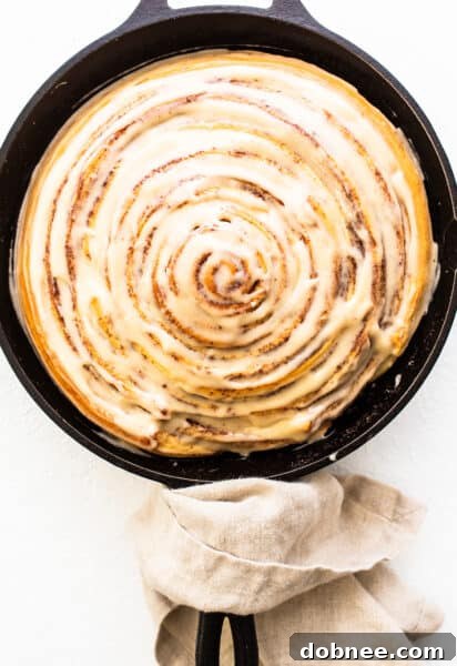 A giant cinnamon roll, perfectly baked and generously frosted with cream cheese icing, ready for presentation.