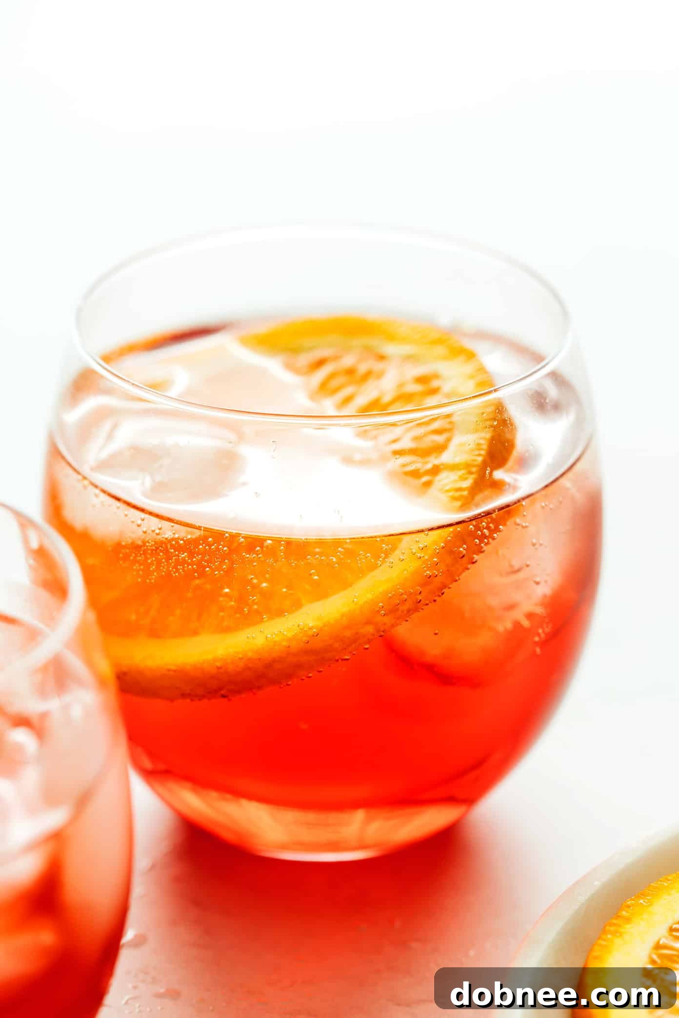 A perfectly prepared Campari Spritz in a stemmed wine glass, garnished with a fresh orange slice, against a soft, bright background.