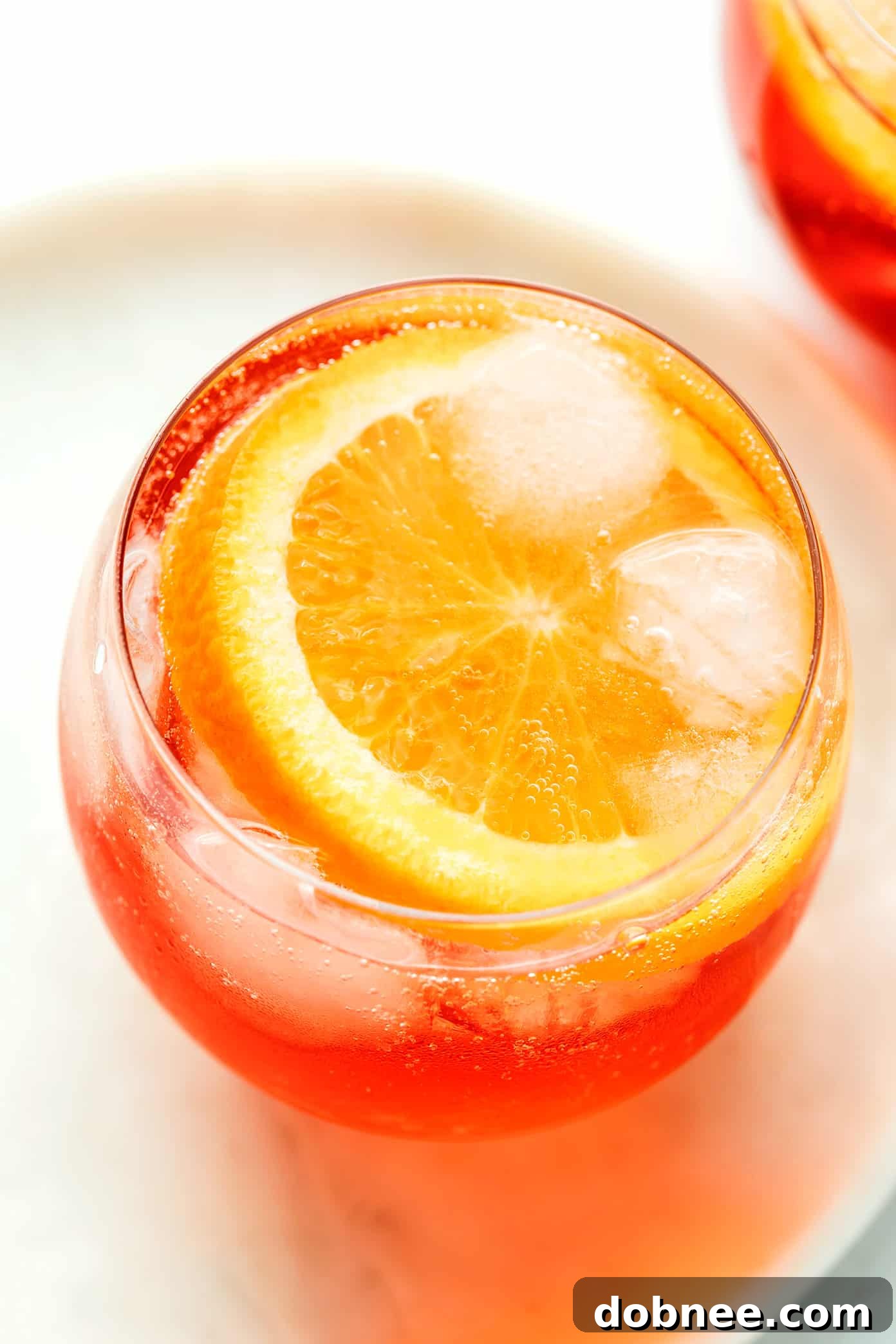 A top-down view of a hand holding a Campari Spritz in a stemmed glass, with an orange slice and sparkling bubbles visible.
