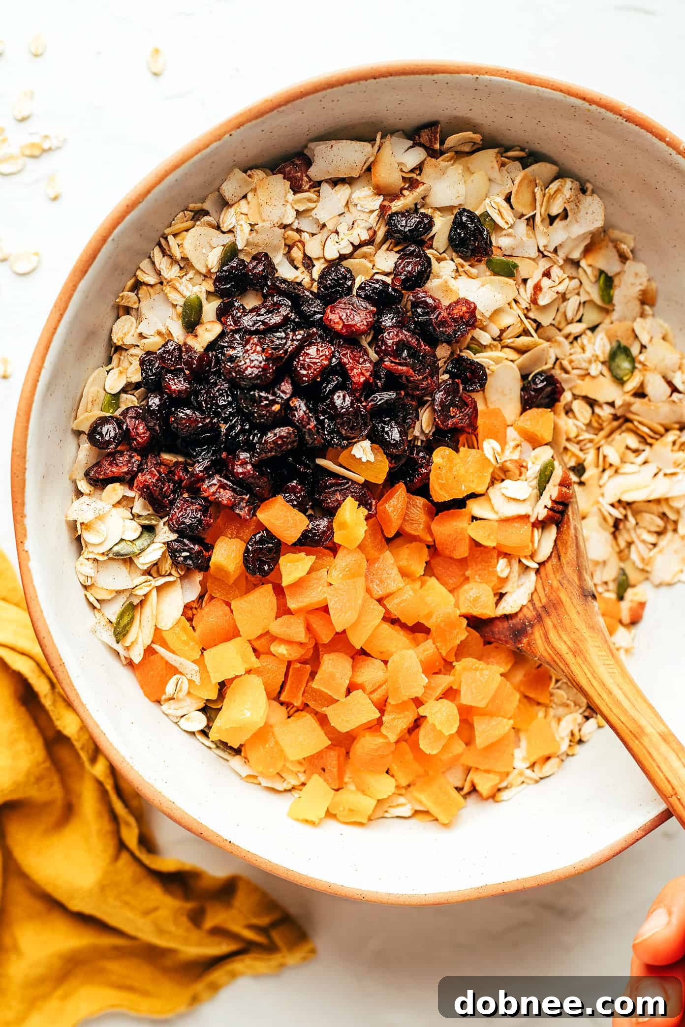 A large mixing bowl filled with homemade muesli ingredients, including oats, toasted nuts, seeds, and dried fruit.