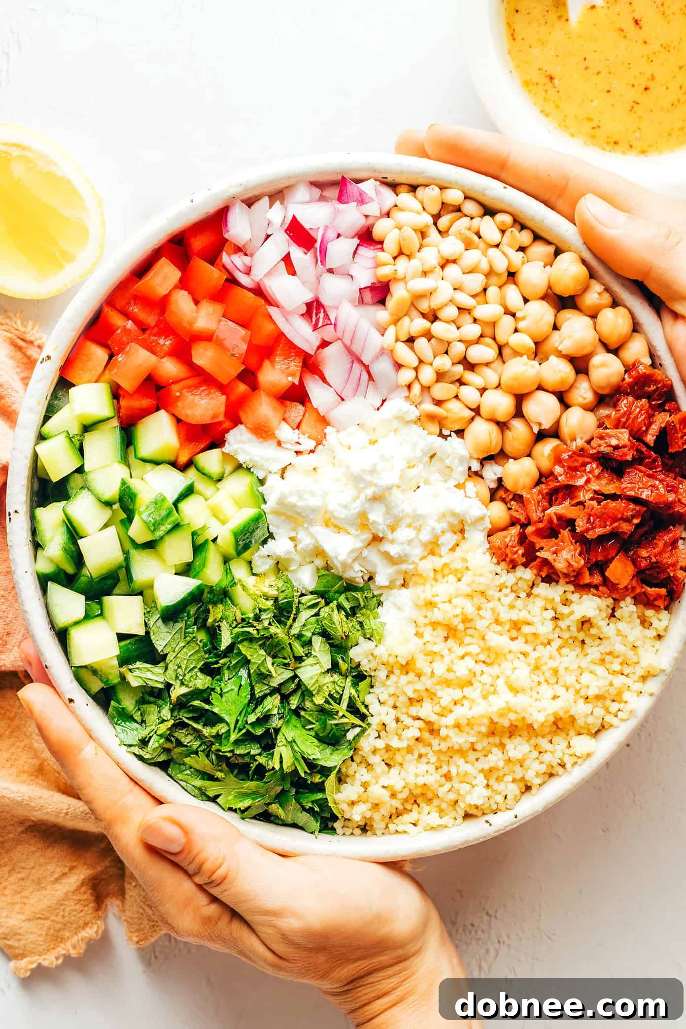 Couscous Salad Ingredients in Bowl - All the vibrant ingredients for the couscous salad, including vegetables, chickpeas, herbs, and feta, artfully arranged in a large mixing bowl before dressing.