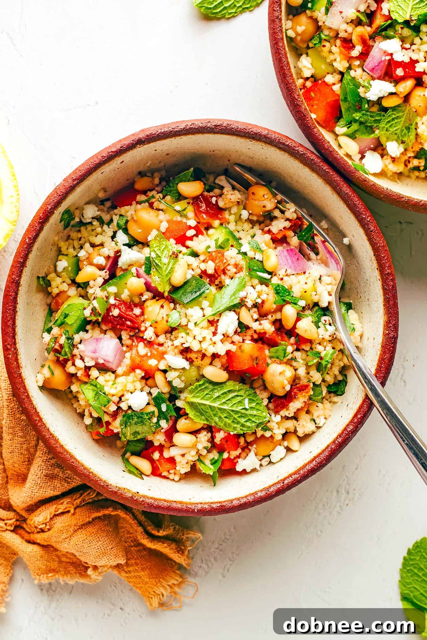 Serving bowls of couscous salad - Two bowls filled with the prepared couscous salad, garnished with fresh herbs, ready to be served. Highlights the vibrant colors and appealing presentation.