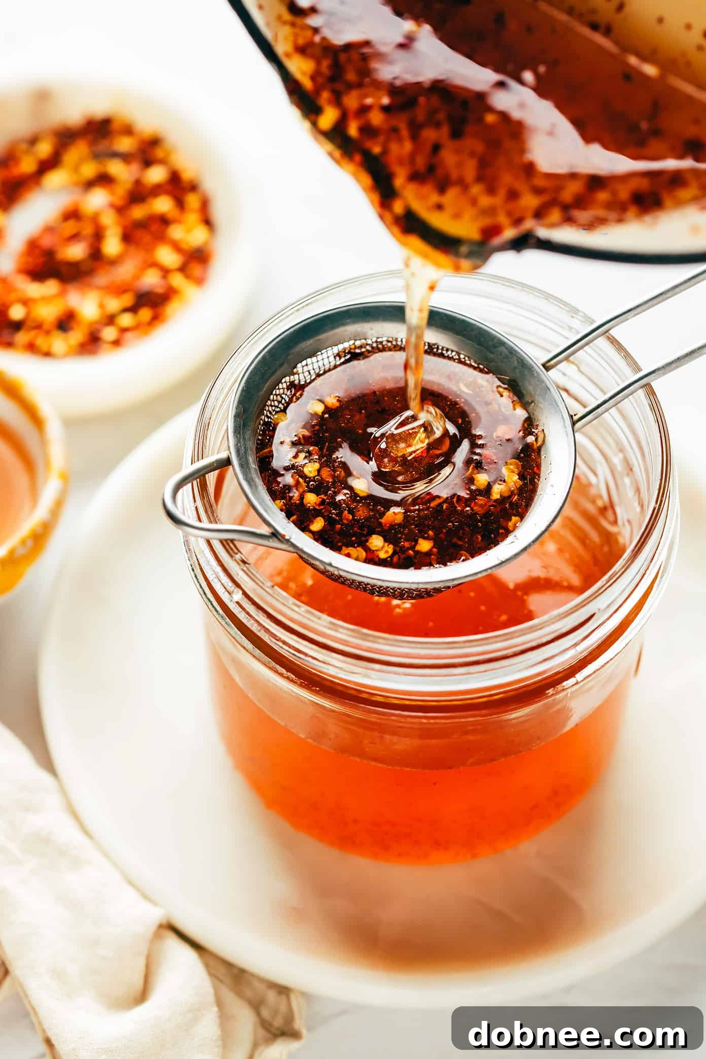This homemade hot honey recipe is quick and easy to make with 3 ingredients and tastes delicious drizzled on everything from pizza to biscuits, fried chicken, salmon, veggies, baked brie and more! | gimmesomeoven.com Straining hot honey into jar through a fine mesh strainer