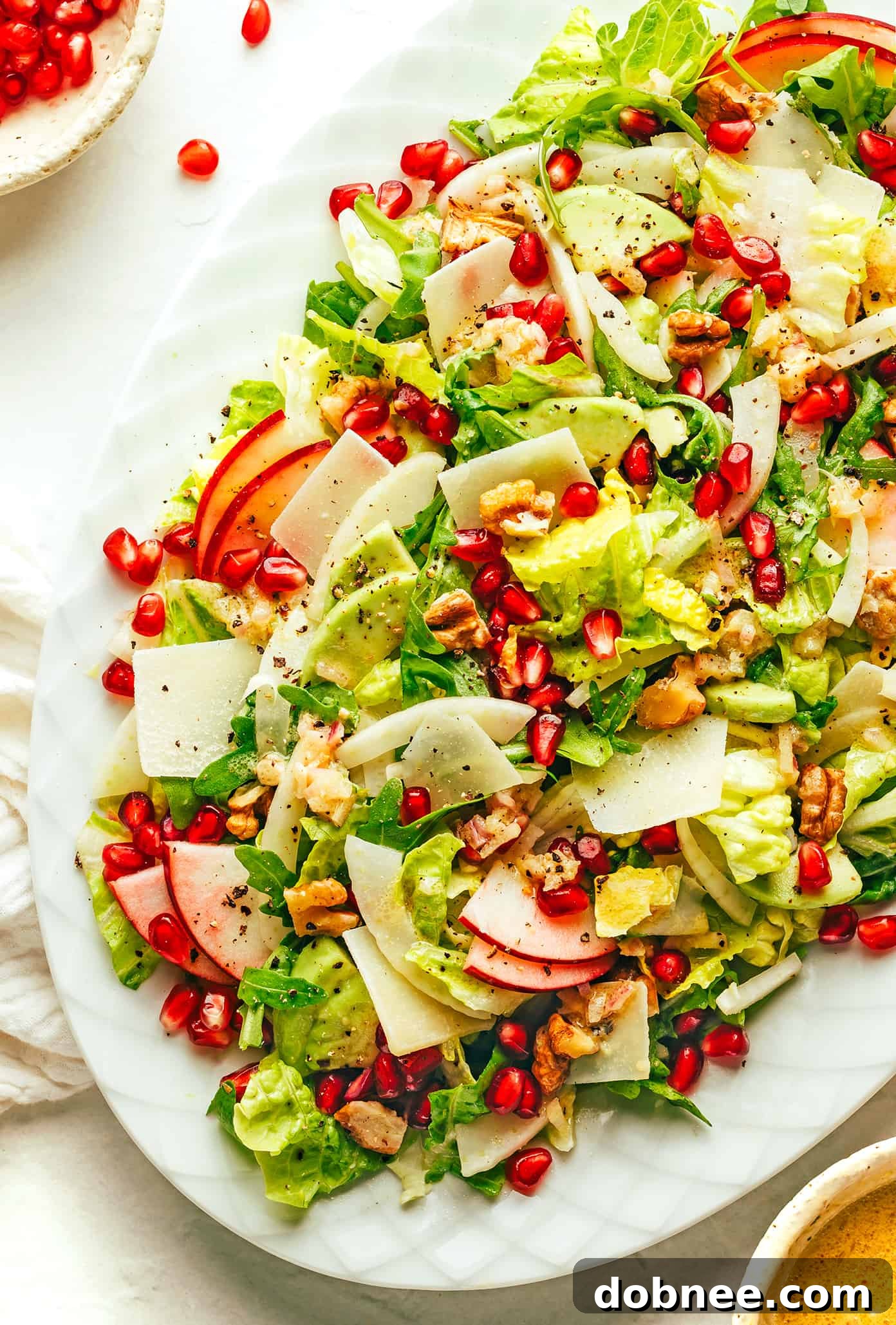 A beautifully presented Favorite Holiday Green Salad with vibrant pomegranates, crisp apple slices, fresh arugula, toasted walnuts, shaved Parmesan, and a light shallot vinaigrette, perfect for festive gatherings.