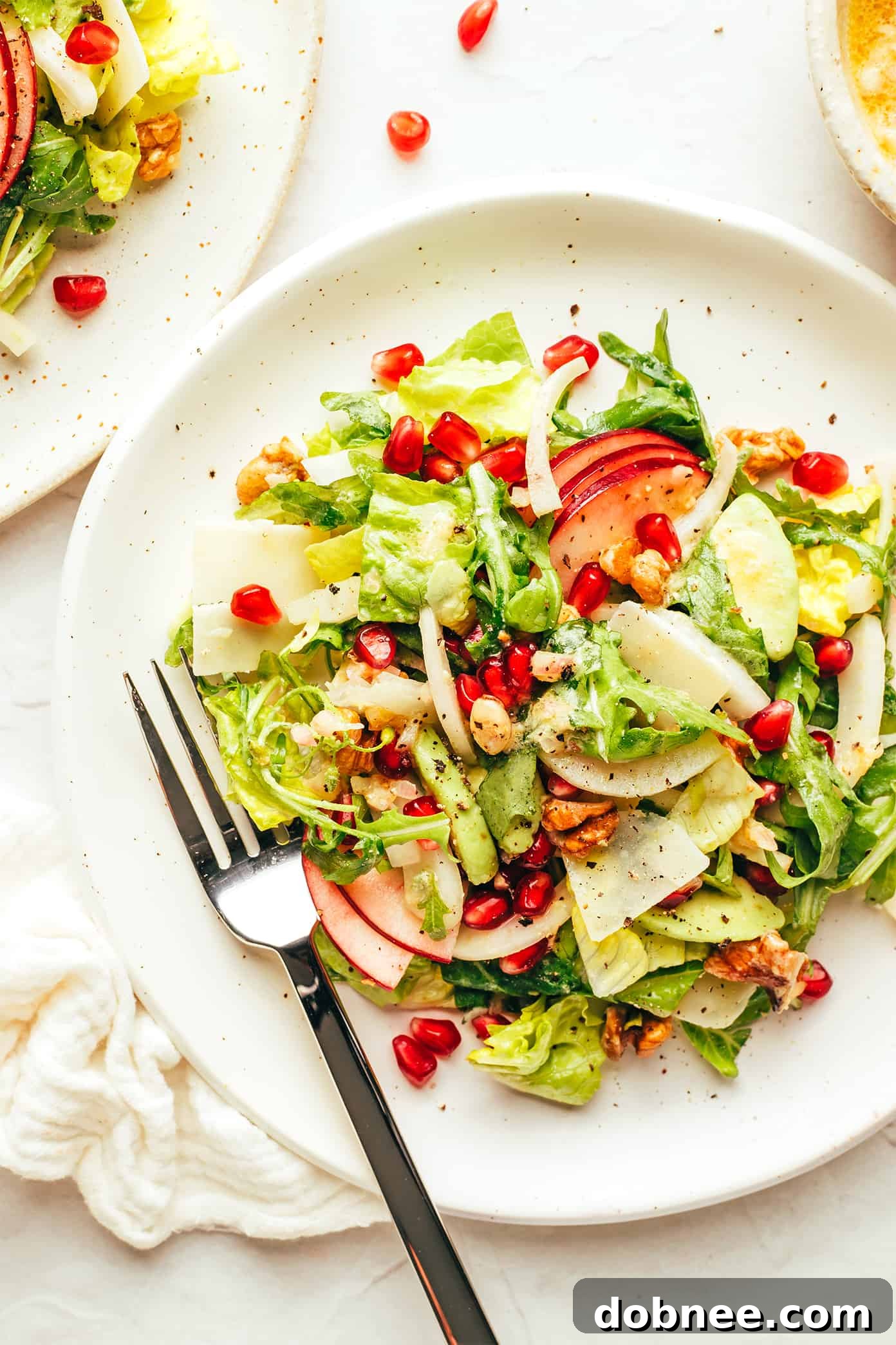 A festive Christmas Salad plated beautifully, showcasing a medley of crisp apple slices, glistening pomegranate arils, savory shaved Parmesan, and crunchy toasted walnuts, ready to be enjoyed.