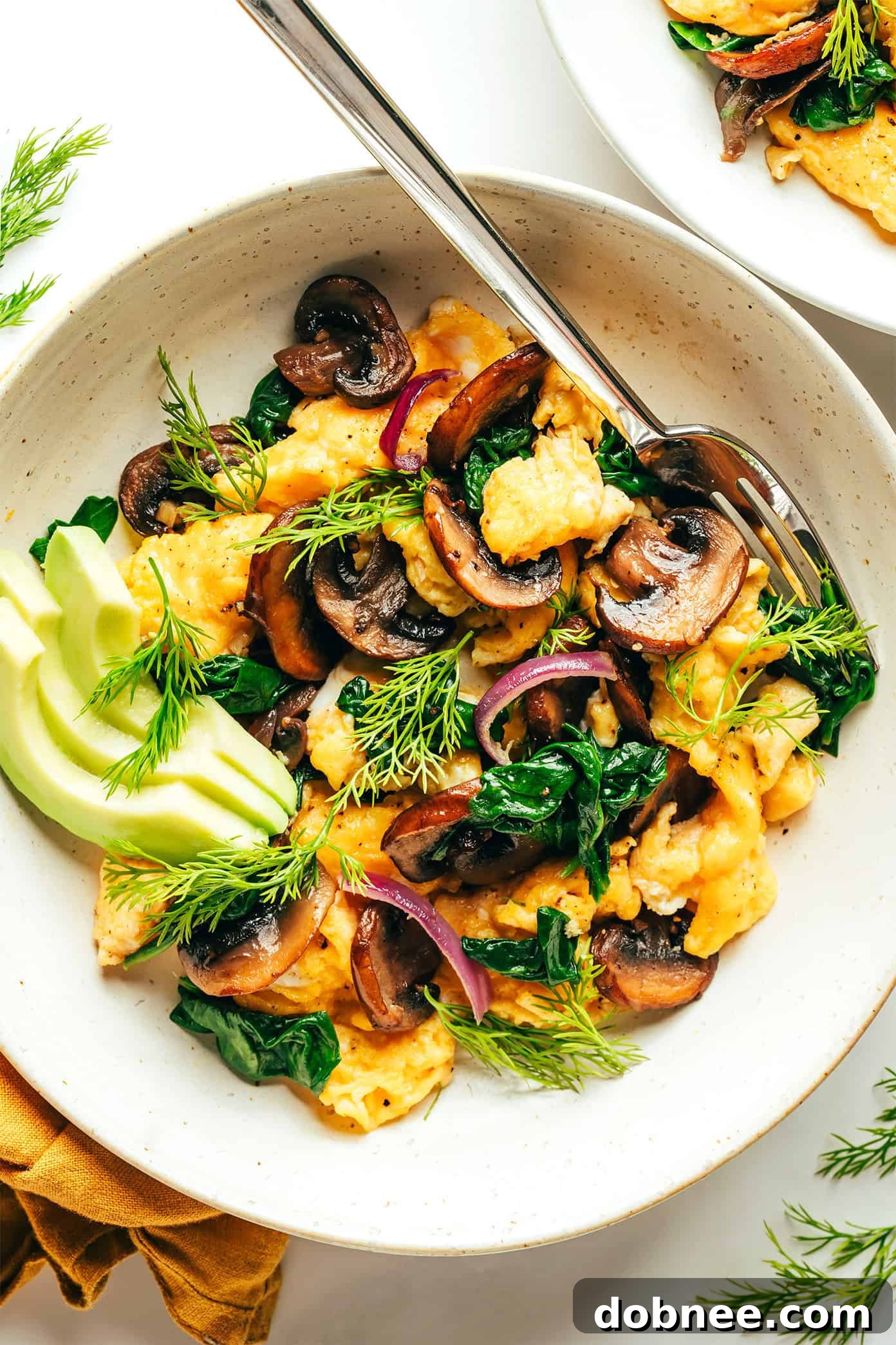 A vibrant bowl of spinach mushroom egg scramble with sliced avocado and fresh herbs, ready to be enjoyed.