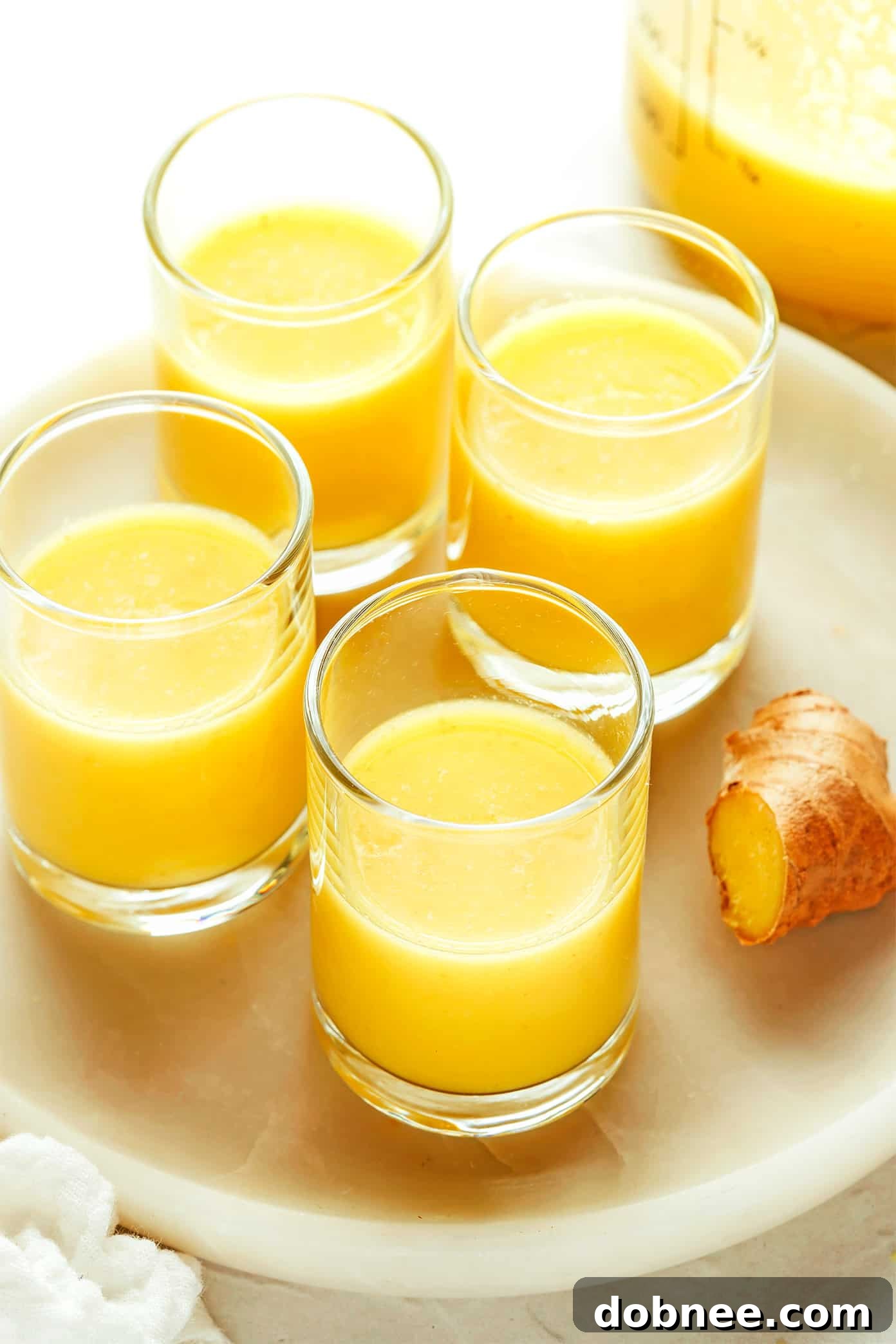 Multiple ginger shots in small glasses, arranged on a rustic wooden surface, ready to be consumed.