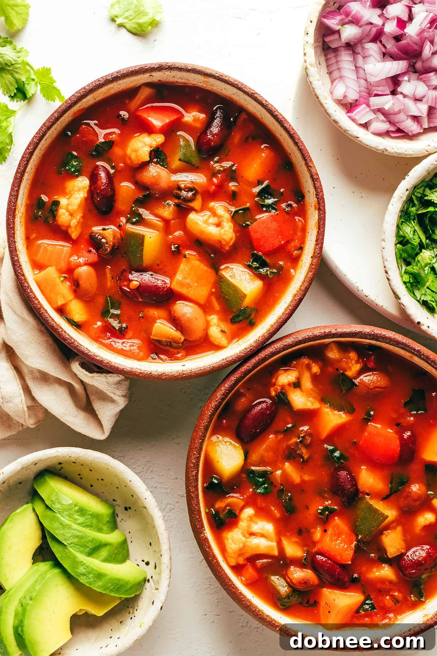 Bowls of extra-veggie vegetarian chili, topped with fresh avocado and cilantro, showcasing a vibrant and delicious plant-based meal.