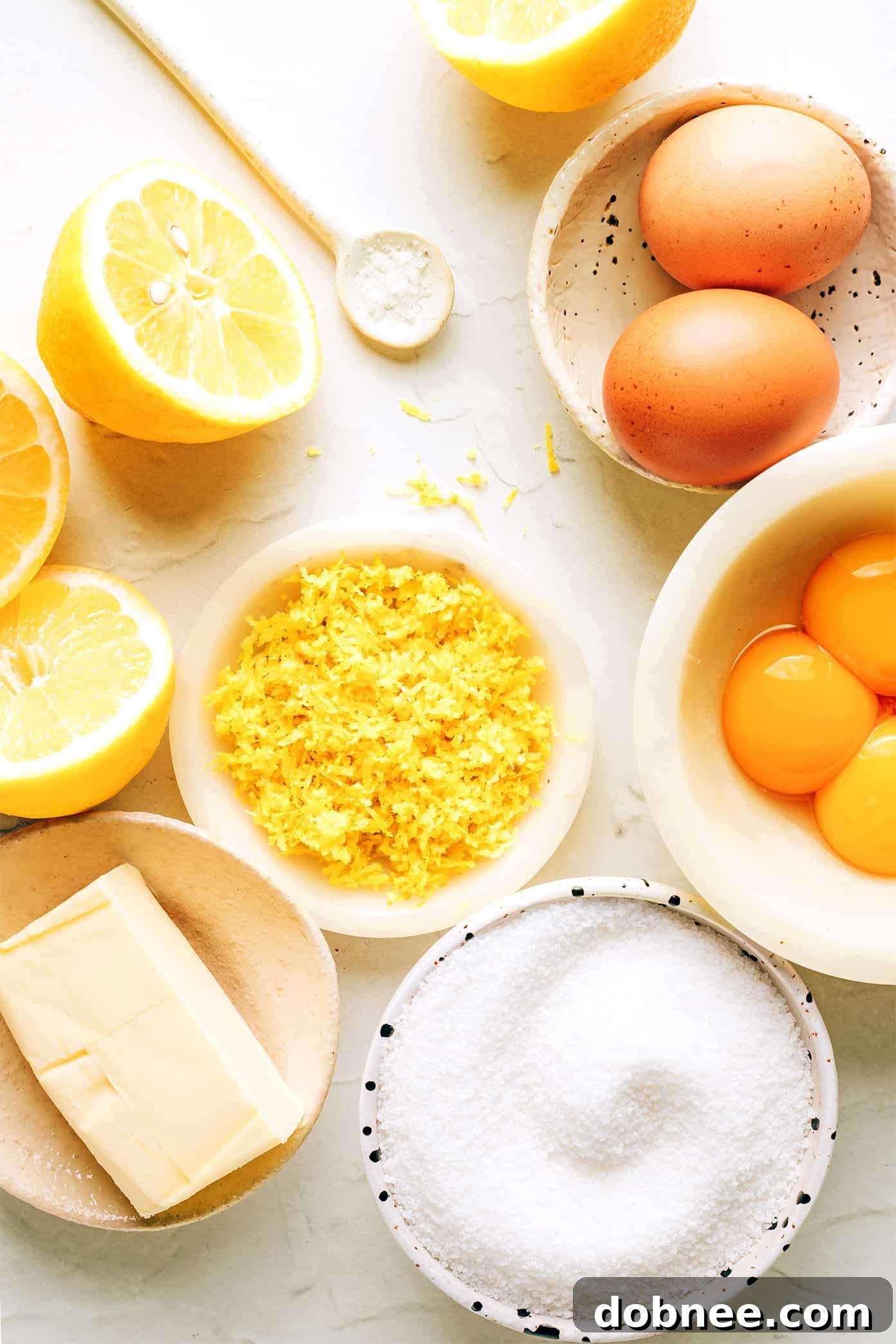 A flat lay photograph showcasing the five simple ingredients required for homemade lemon curd: fresh lemons, eggs, granulated sugar, butter, and a pinch of salt.