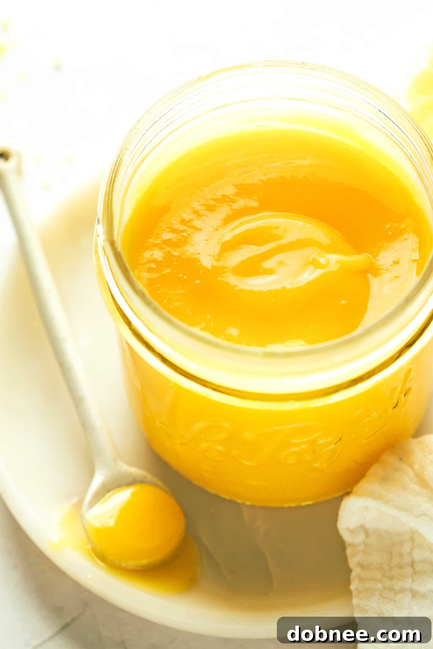 A charming glass jar filled with vibrant homemade lemon curd, a spoon resting beside it, inviting a taste.