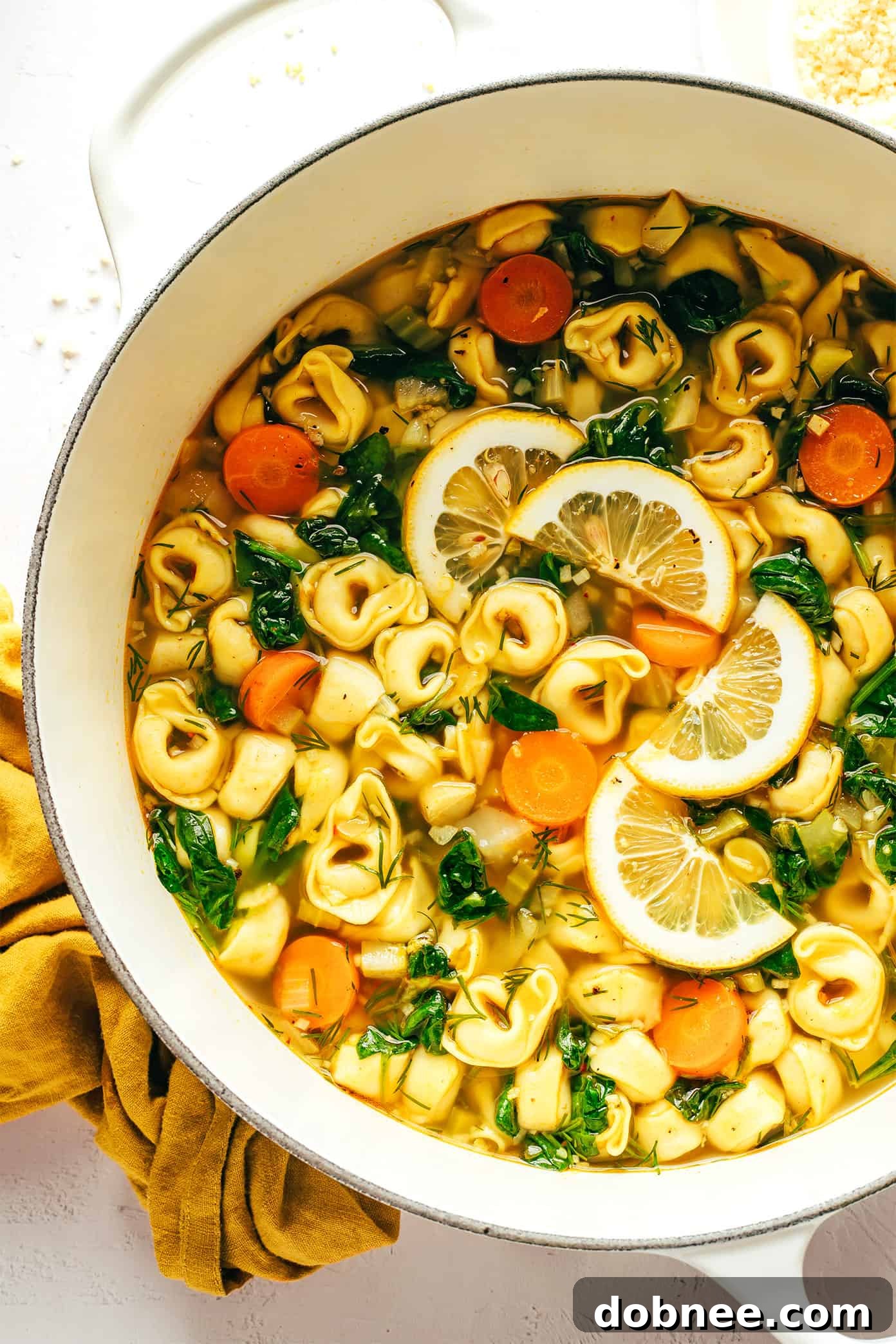 A bowl of Lemony Tortellini Soup garnished with fresh dill and Parmesan cheese.