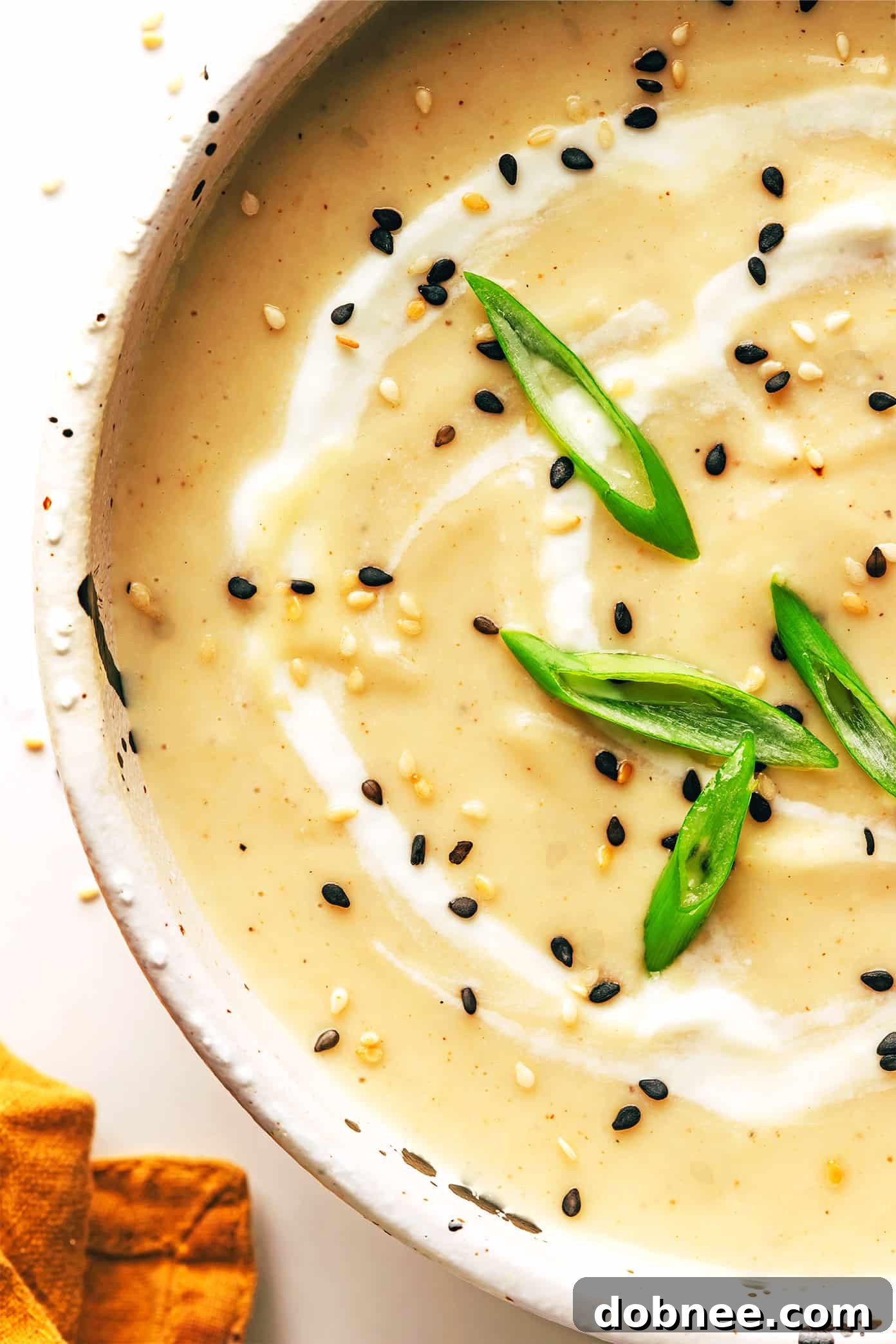 A top-down view of a large pot of creamy sesame ginger roasted cauliflower soup with fresh toppings.