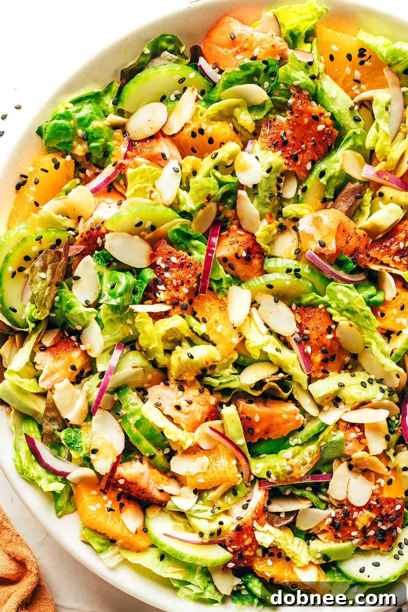 Vibrant Orange Salmon Salad with Avocado, Cucumber, Red Onion, Toasted Almonds, and Romaine Lettuce, Drizzled with Ginger Hot Honey Vinaigrette