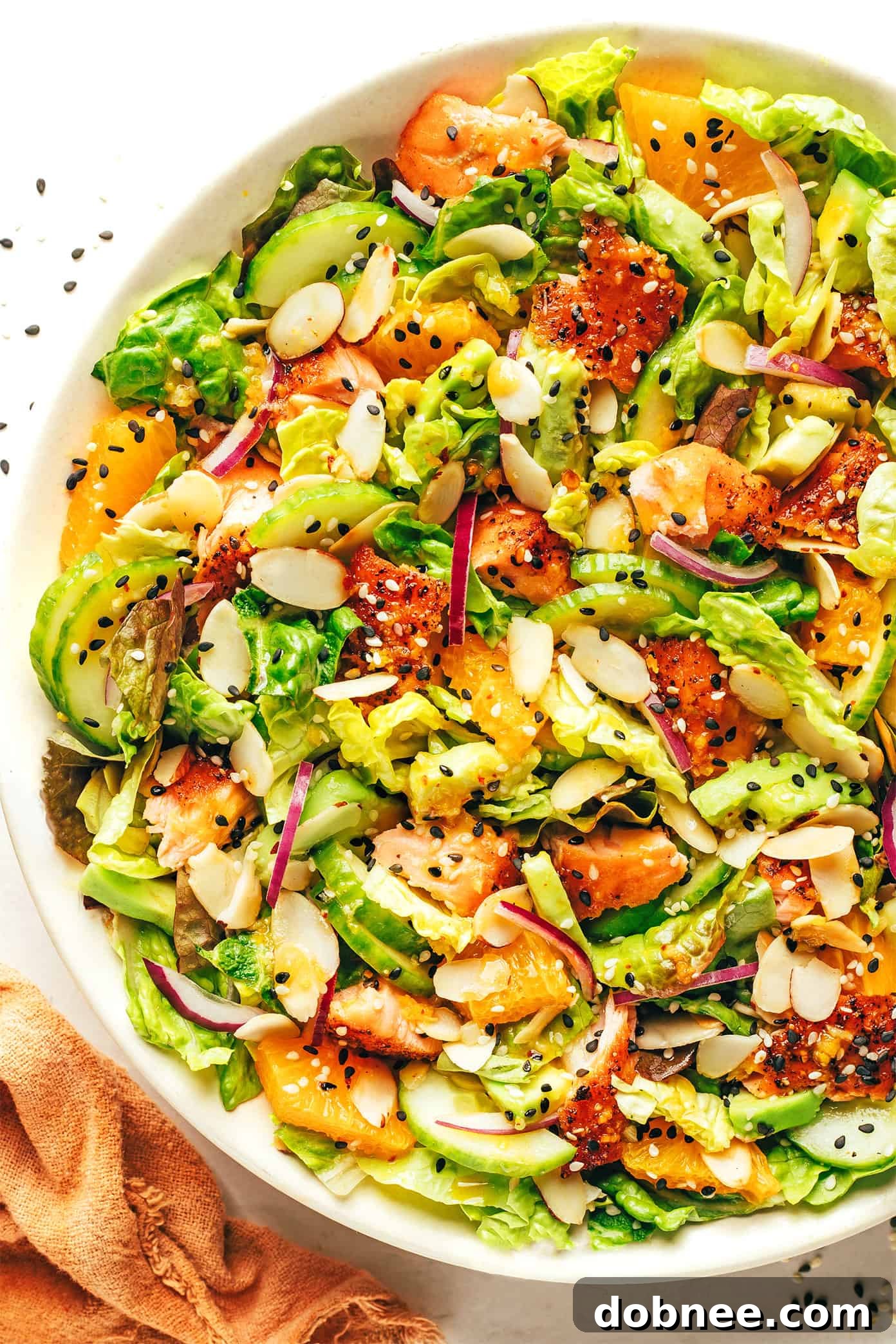 Orange salmon salad with creamy avocado and crunchy toasted almonds in a serving bowl