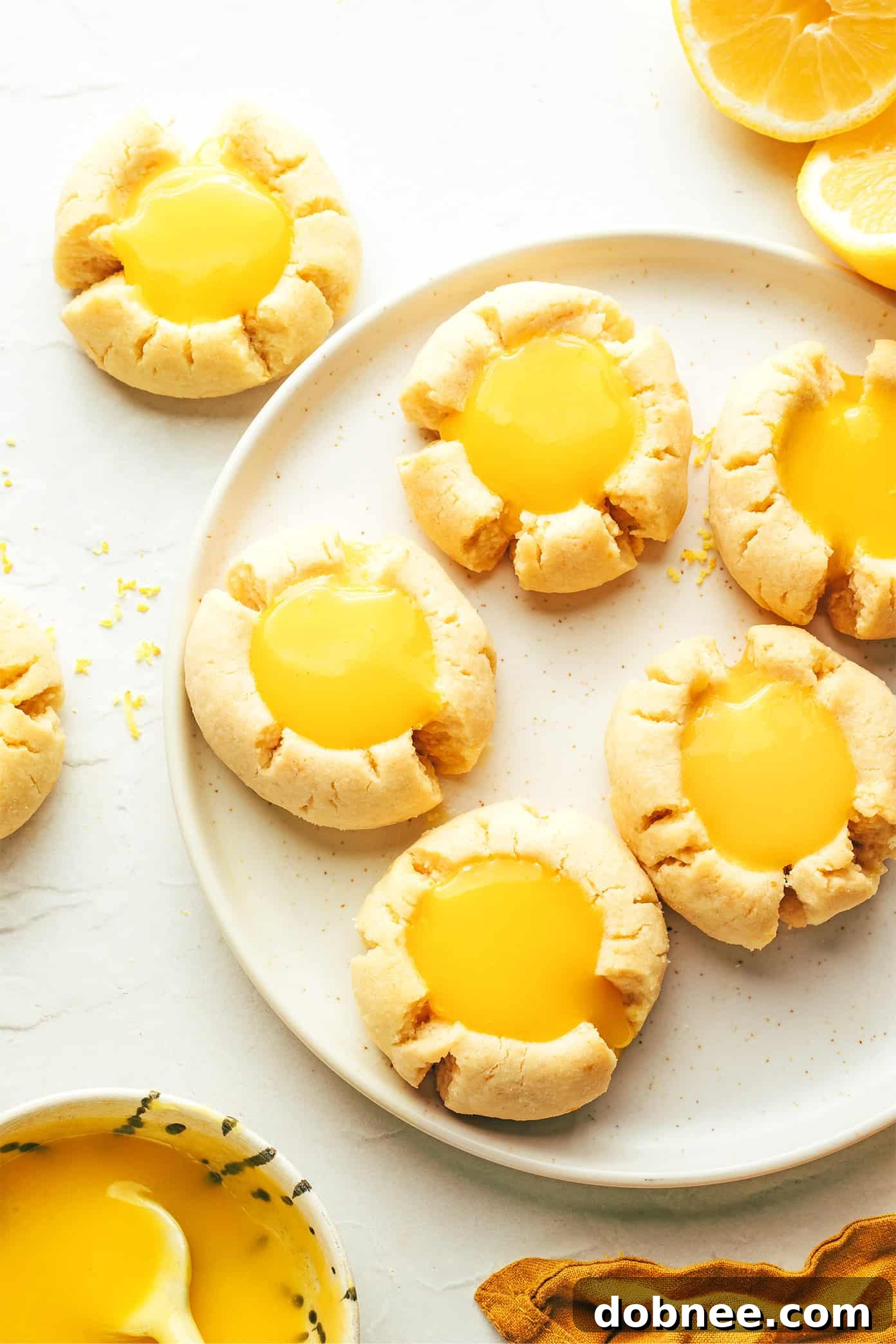 A plate of fresh lemon thumbprint cookies garnished with extra lemon curd and fresh lemon slices