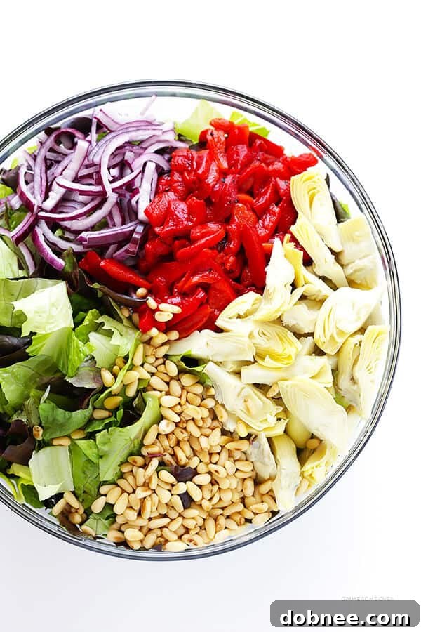 Our Family's Favorite Salad is made with lots of artichoke hearts, roasted red peppers, toasted pine nuts, and a zesty Parmesan vinaigrette. SO delicious, and always a crowd pleaser! | gimmesomeoven.com