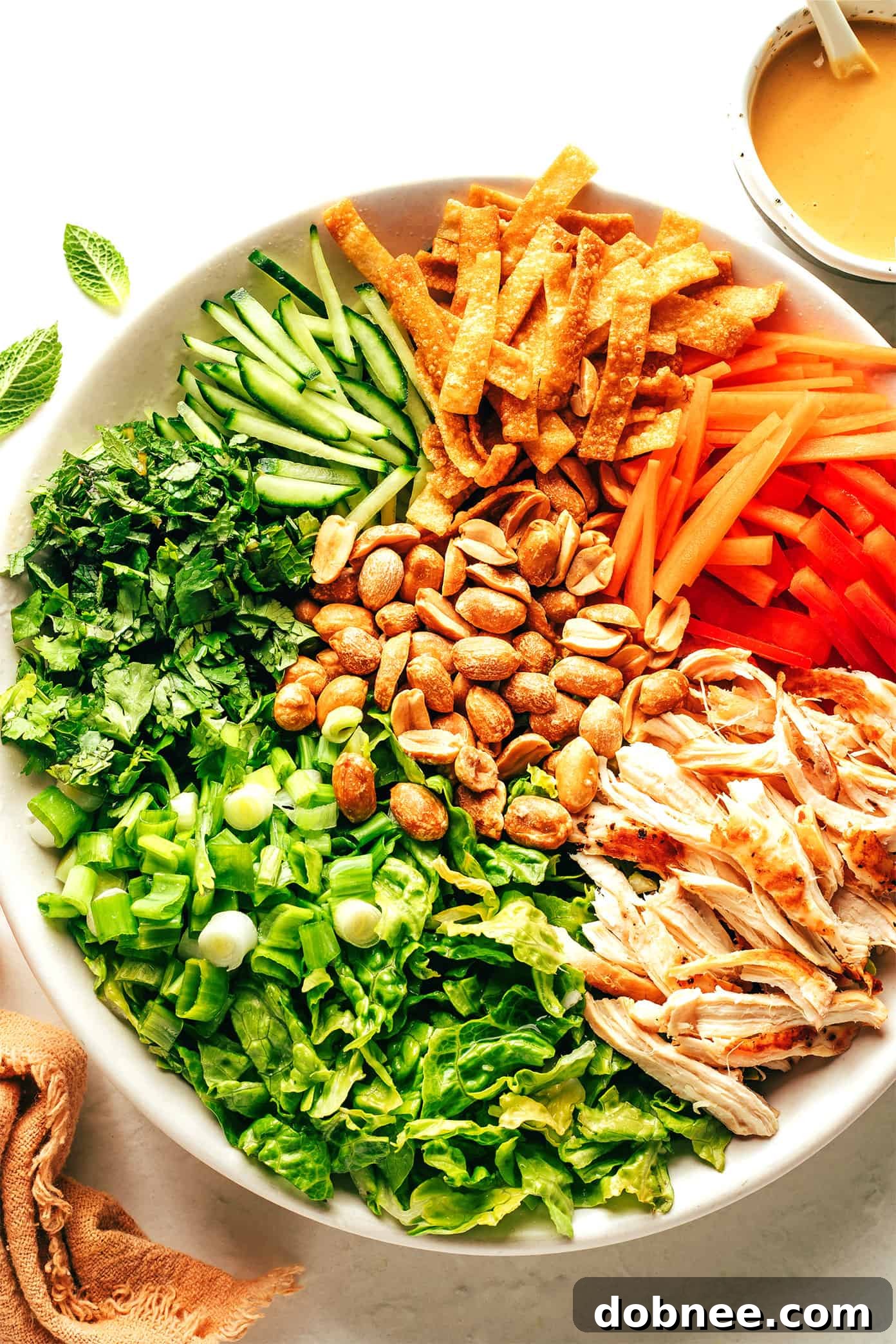 All the chopped salad ingredients, including chicken, cabbage, various vegetables, and wontons, mixed together in a large serving bowl before the dressing is added.
