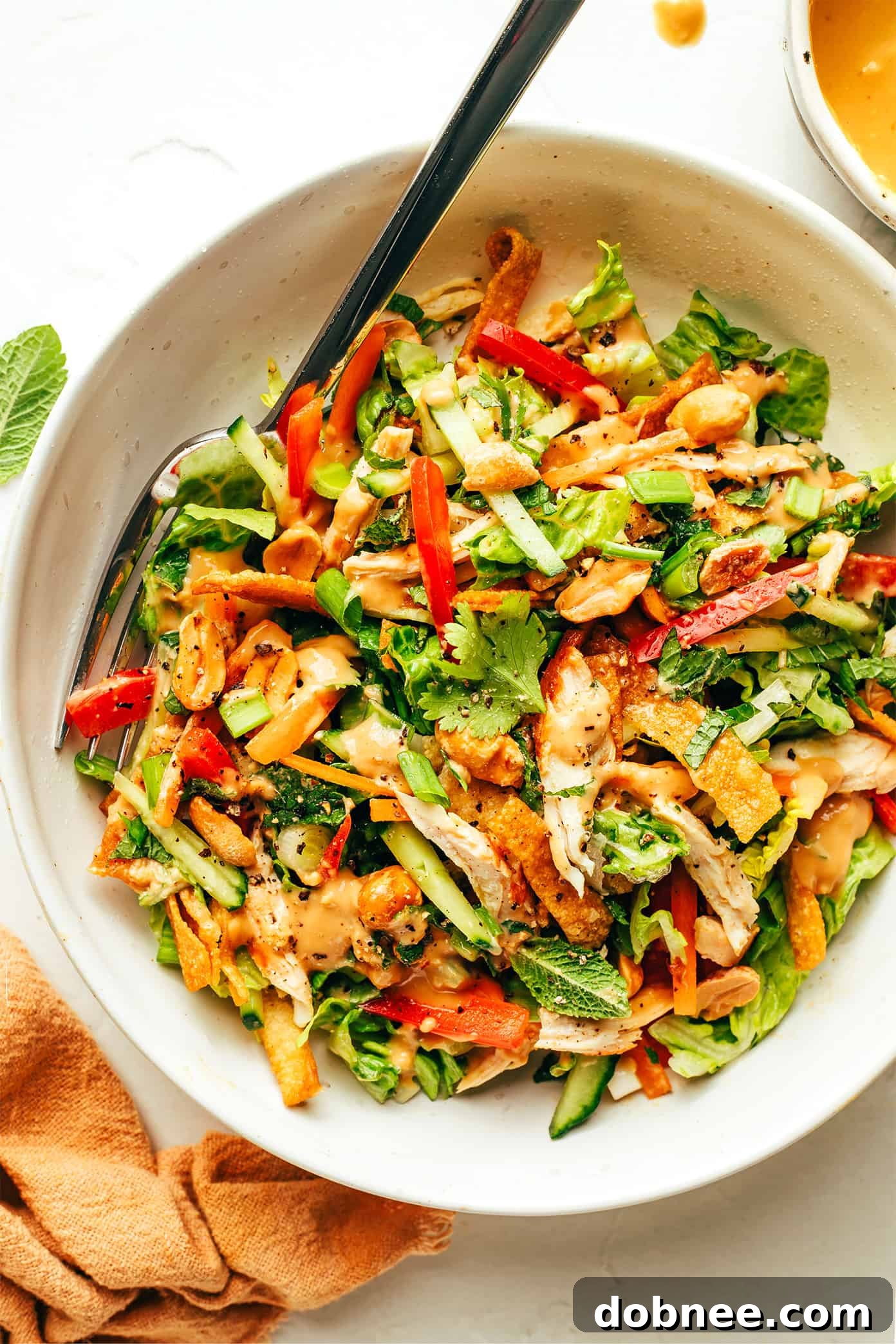A fork digging into a fresh, colorful Thai Crunch Salad, showcasing the layers of ingredients and rich peanut dressing.