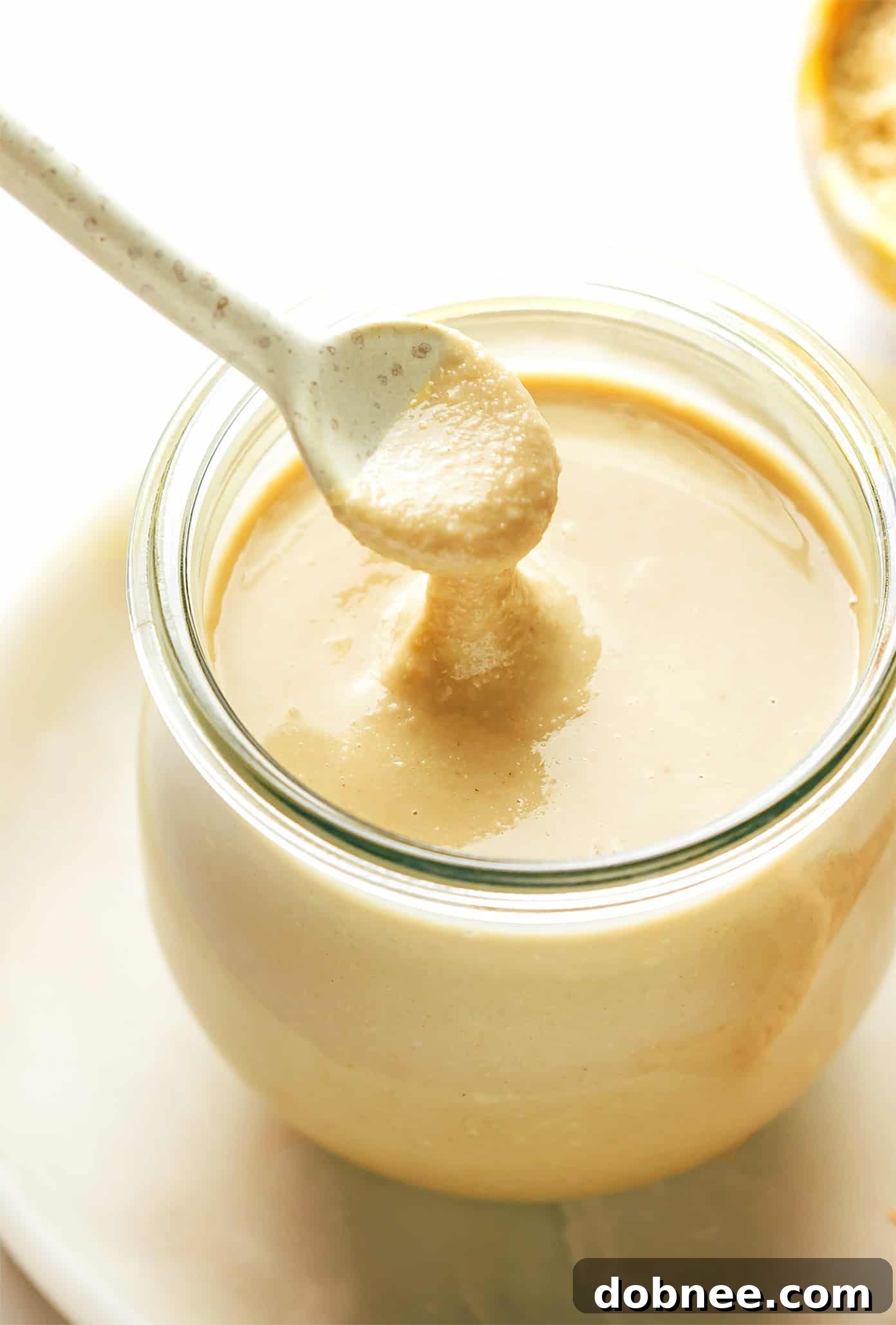 A glass jar filled with freshly made homemade tahini, showcasing its creamy, light brown texture.
