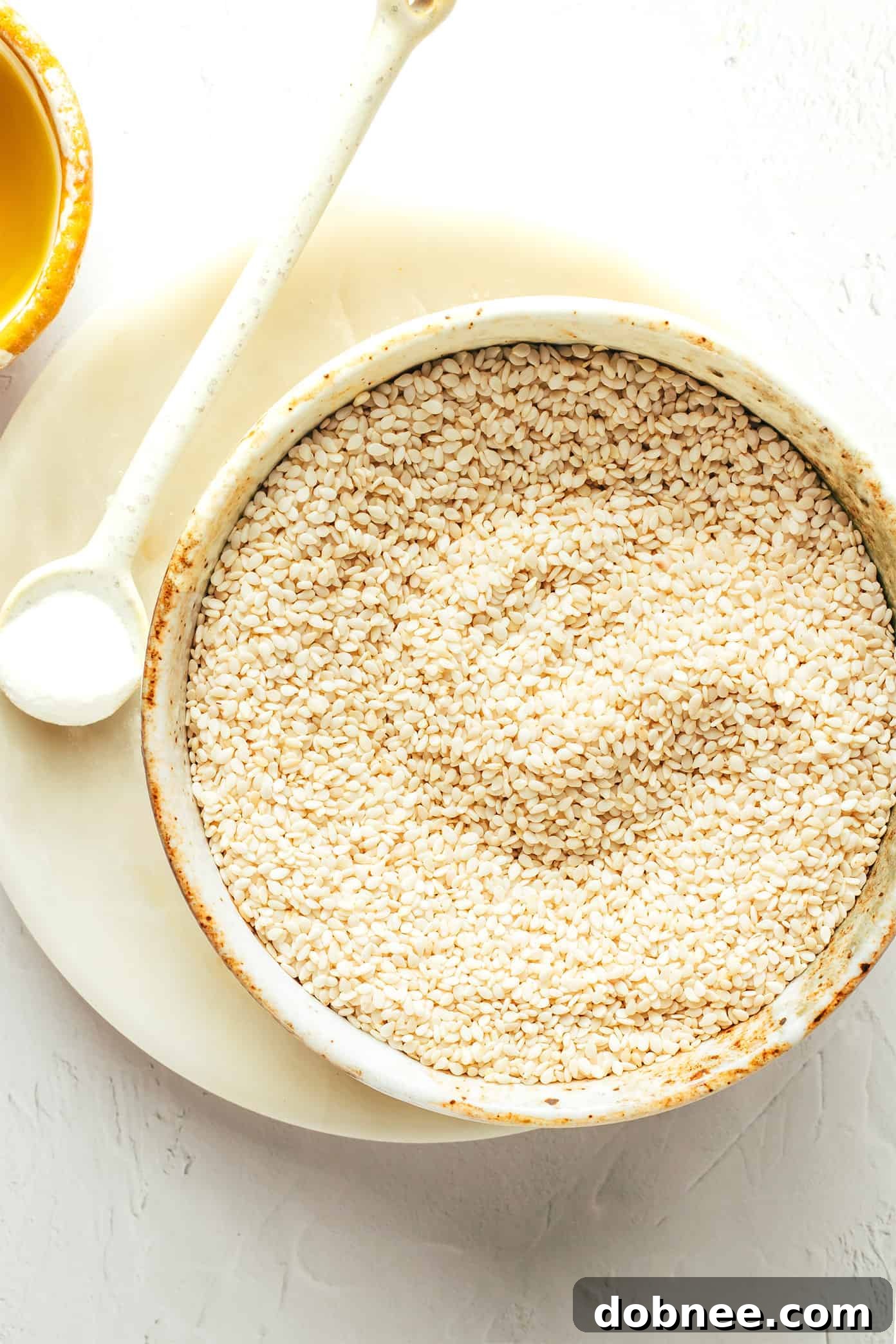 Three essential ingredients for homemade tahini: a bowl of raw sesame seeds, a bottle of olive oil, and a small dish of sea salt.