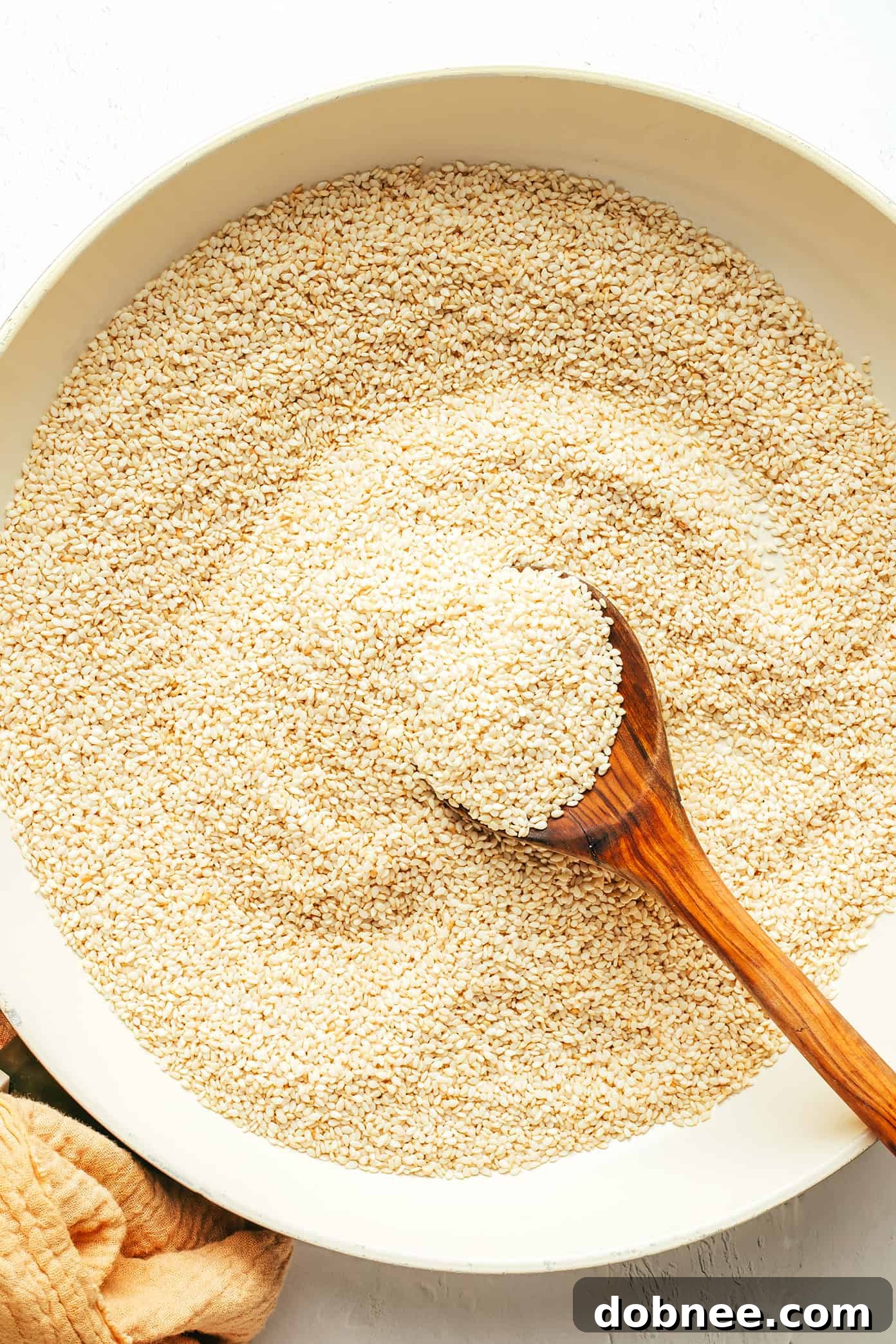 Sesame seeds being lightly toasted in a sauté pan on a stovetop, a crucial step for making flavorful homemade tahini.
