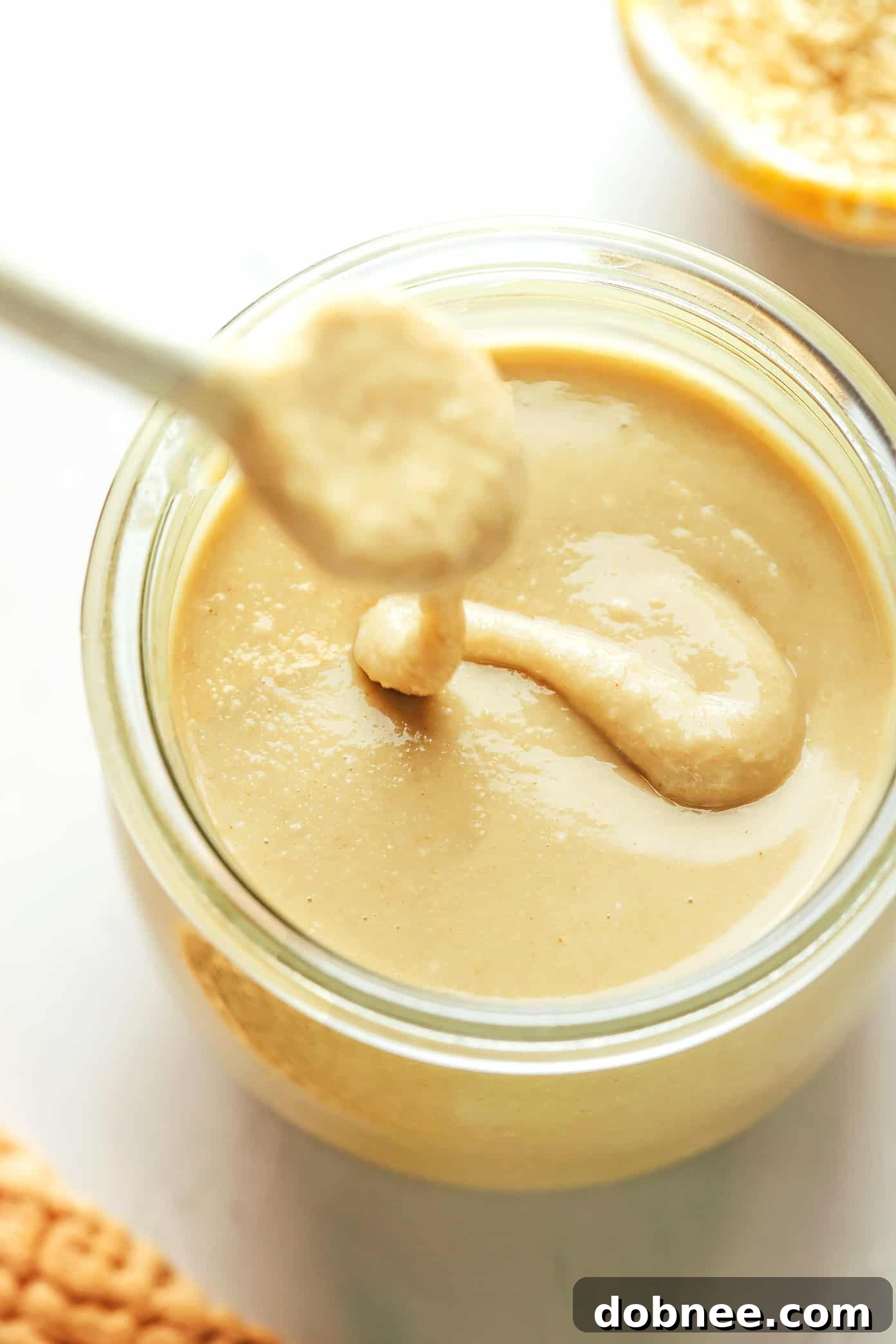 Freshly made homemade tahini being drizzled into a clean glass jar, showing its smooth, pourable consistency.