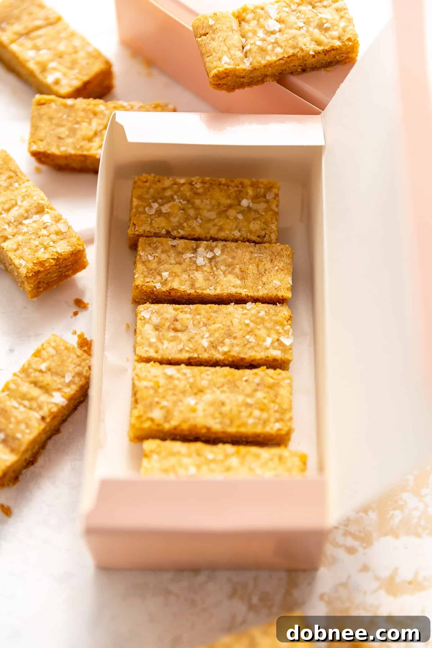 Stack of golden shortbread bars with flaky sea salt on a rustic wooden board