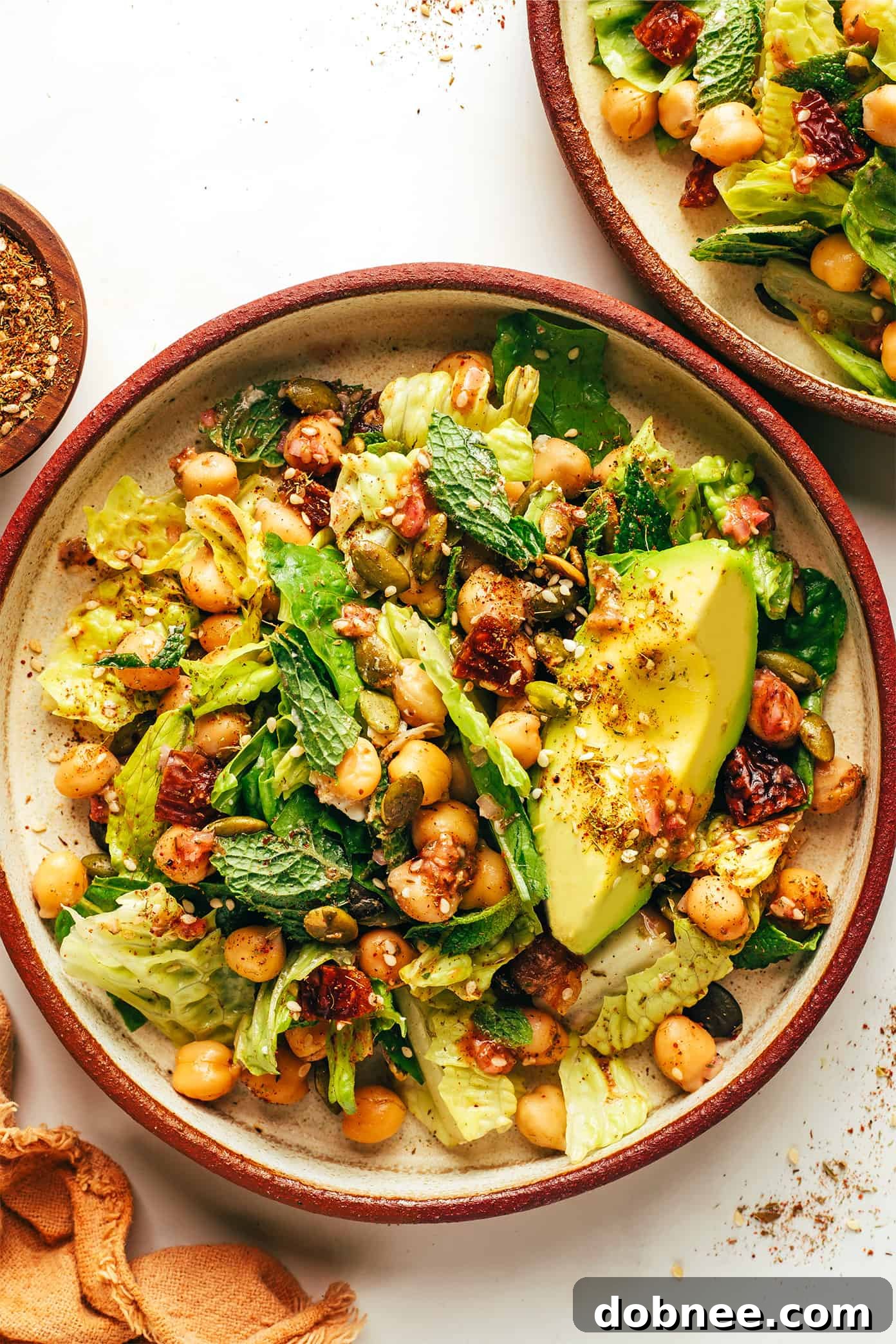 A beautifully presented bowl of Chickpea, Date, and Avocado Salad with Za'atar Vinaigrette, showcasing its fresh green color and diverse ingredients.