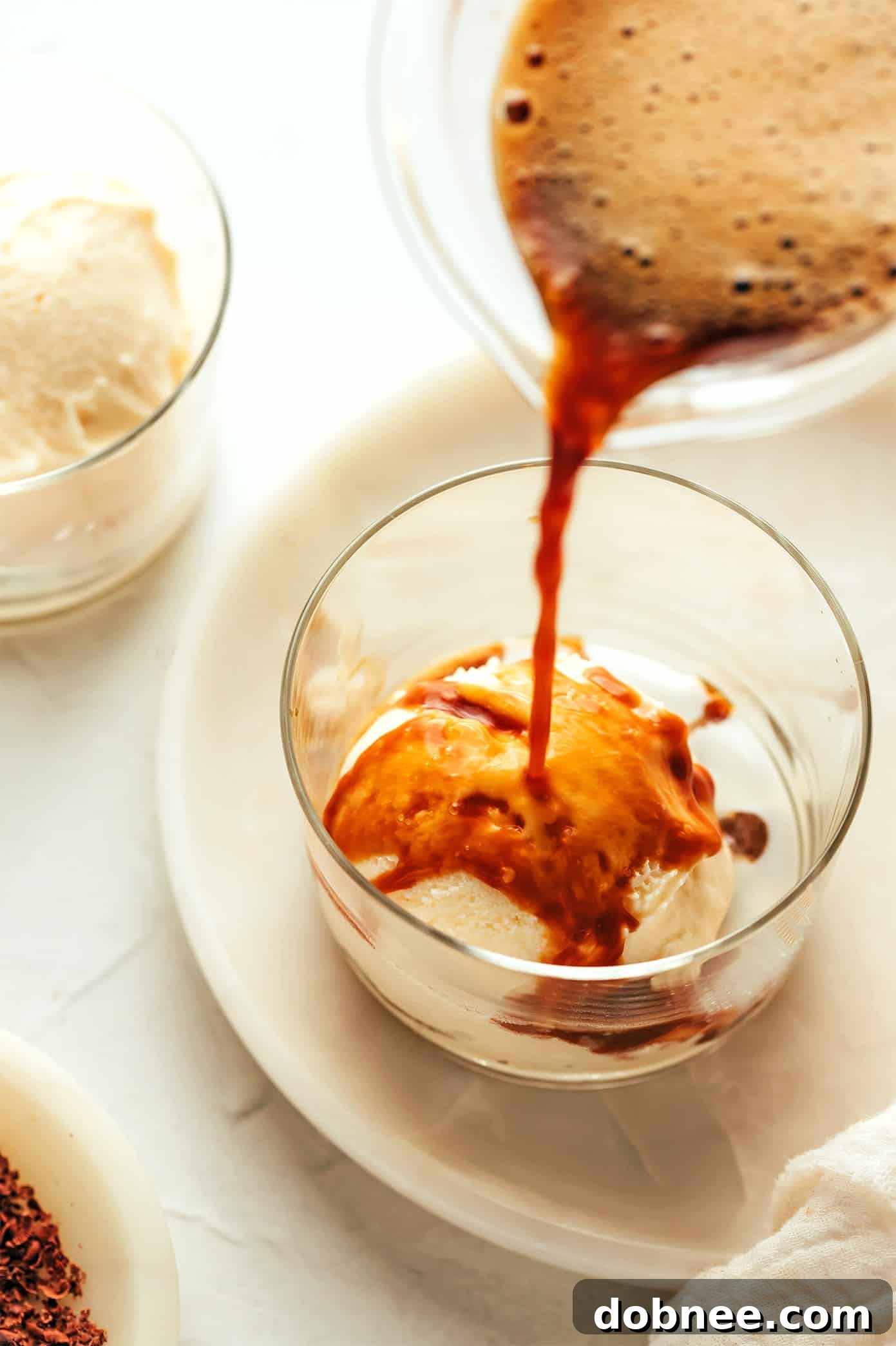 Ingredients for affogato laid out: a coffee maker, a cup of espresso, a tub of vanilla ice cream, and chocolate bar for shavings.