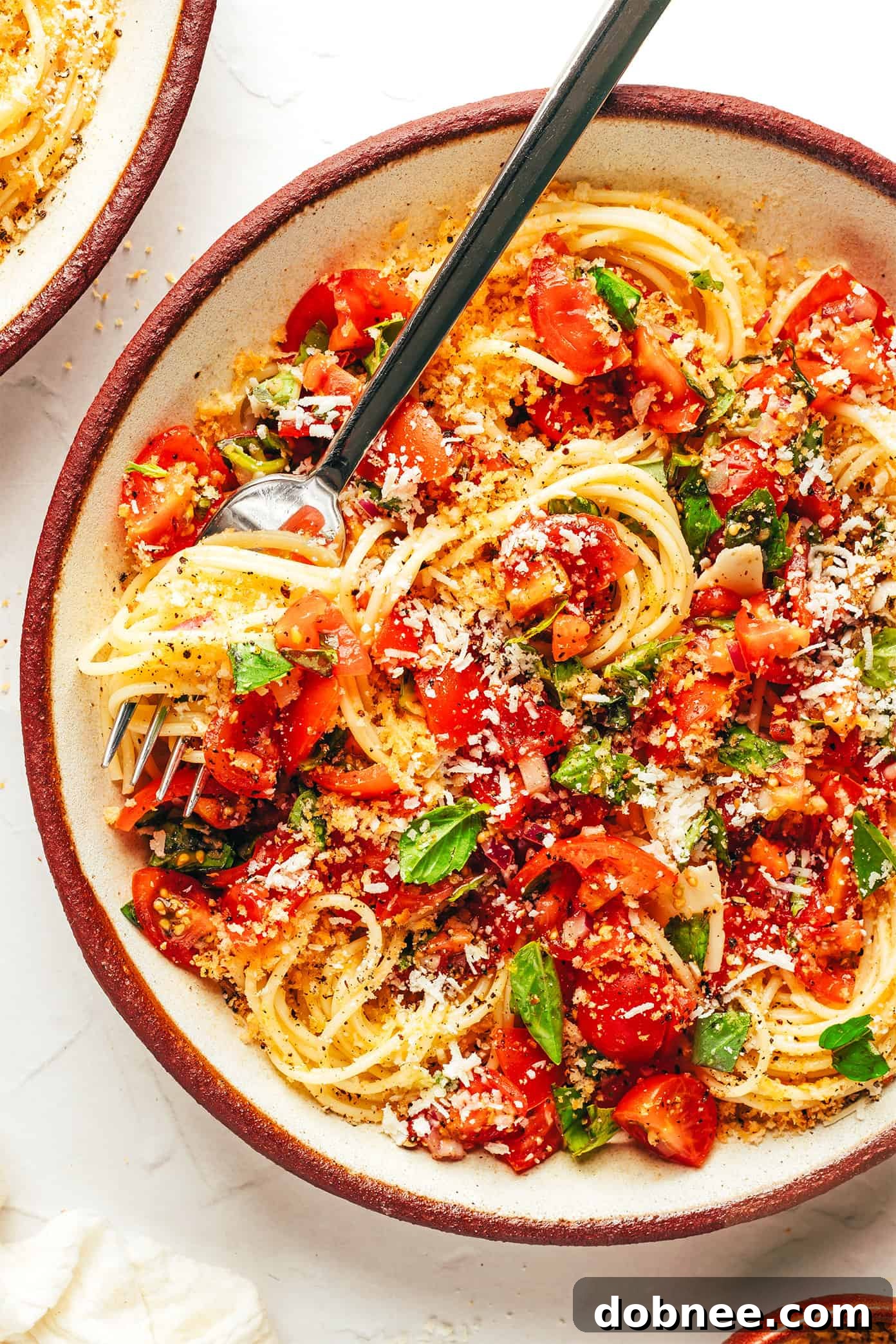 A close-up of Fresh Bruschetta Pasta in a bowl, showing the texture and fresh ingredients, garnished with basil and breadcrumbs.