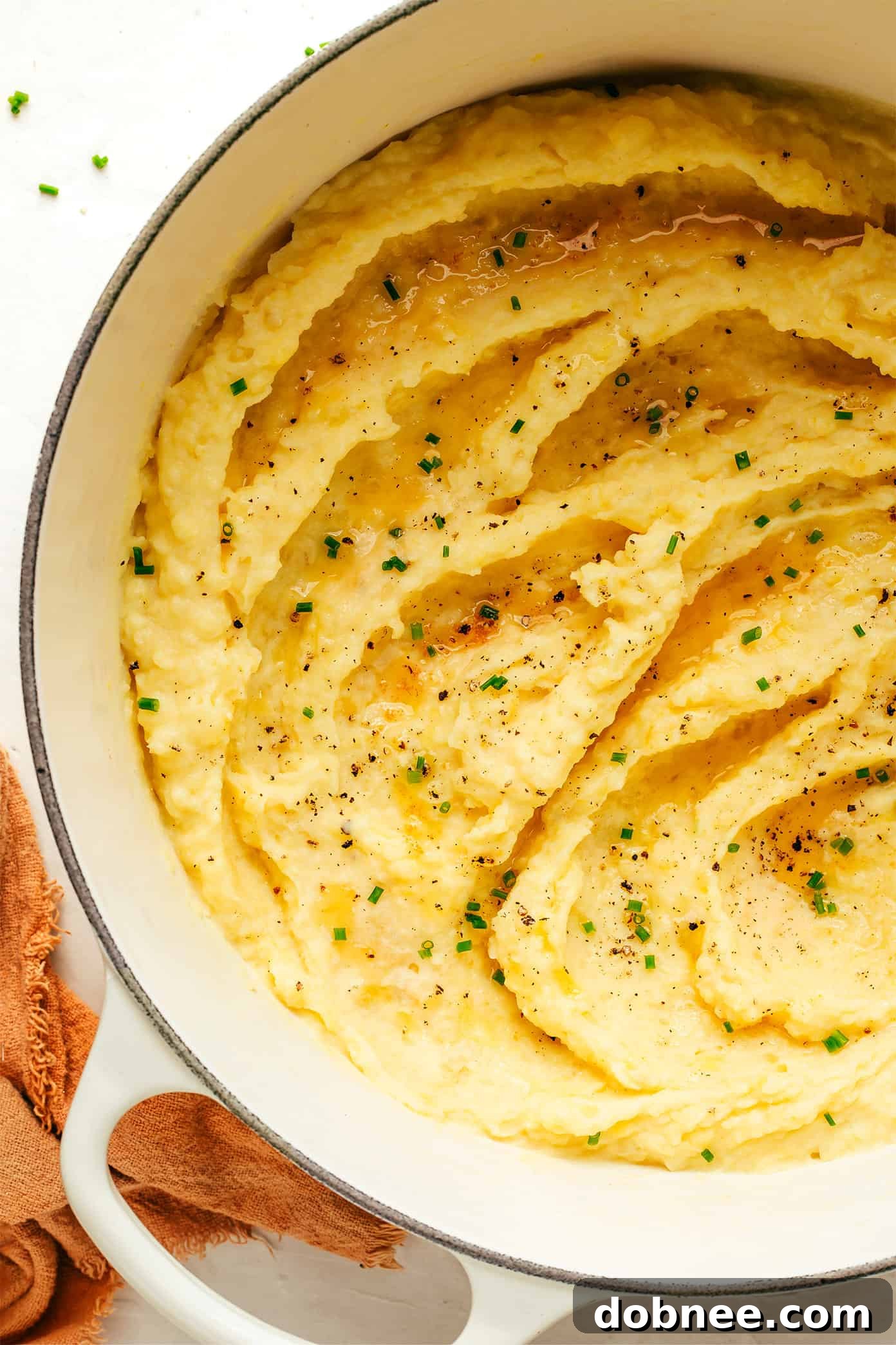 A bowl of brown butter mashed potatoes, garnished with fresh herbs, ready for serving on a wooden table.