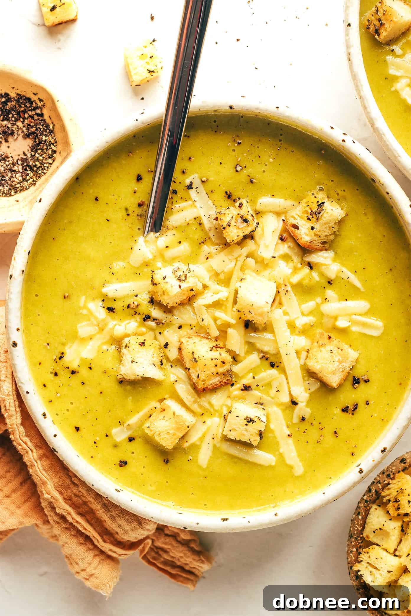 A steaming bowl of lightened-up broccoli cheese soup, garnished with croutons and fresh herbs, perfect for a cozy meal.