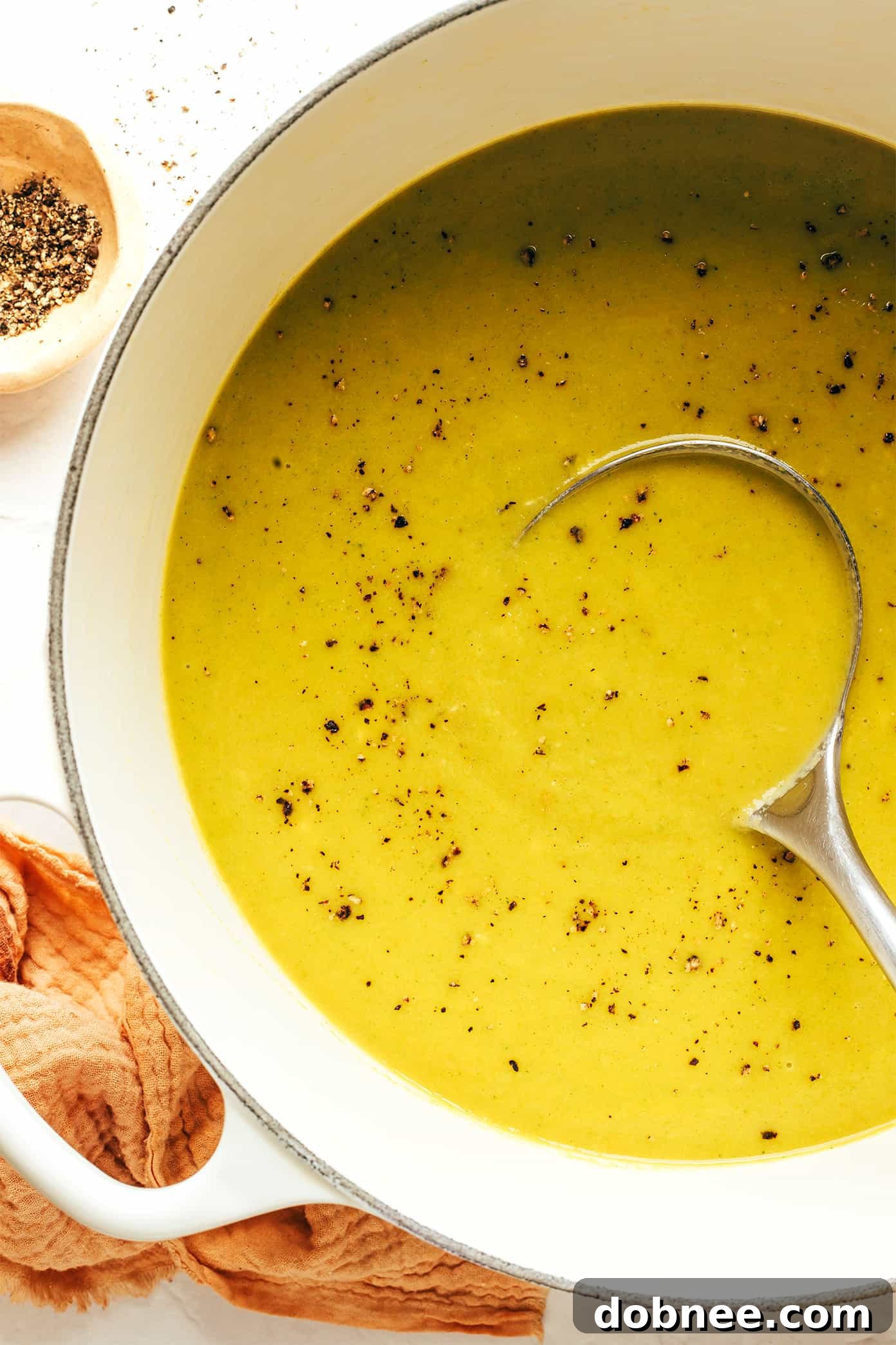 A vibrant, delicious bowl of lightened-up broccoli cheese soup, ready to be enjoyed, with a spoon dipping in, on a wooden table.