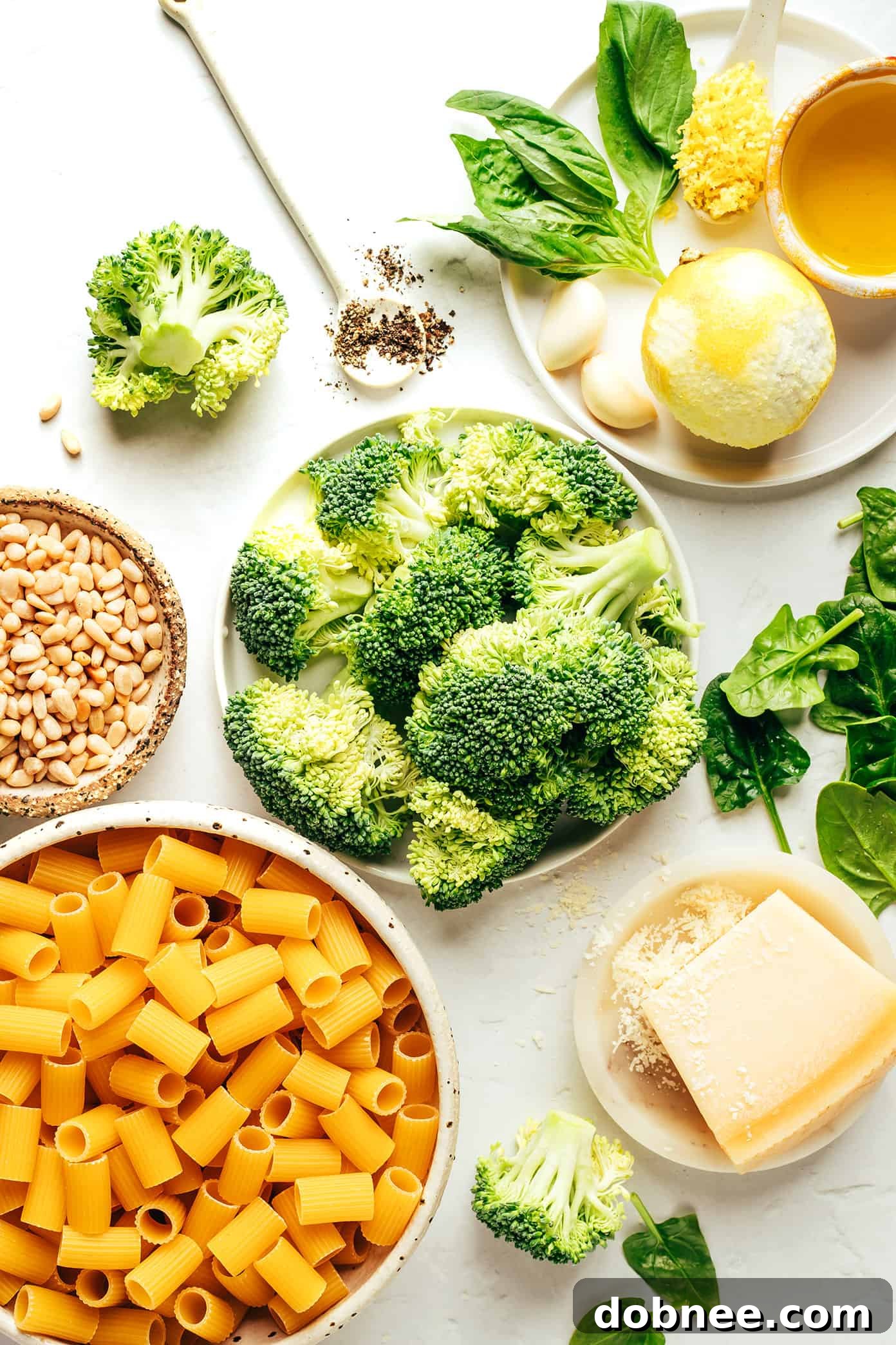 Close-up shot of the fresh ingredients for broccoli pesto, including basil, spinach, lemon, and Parmesan cheese.