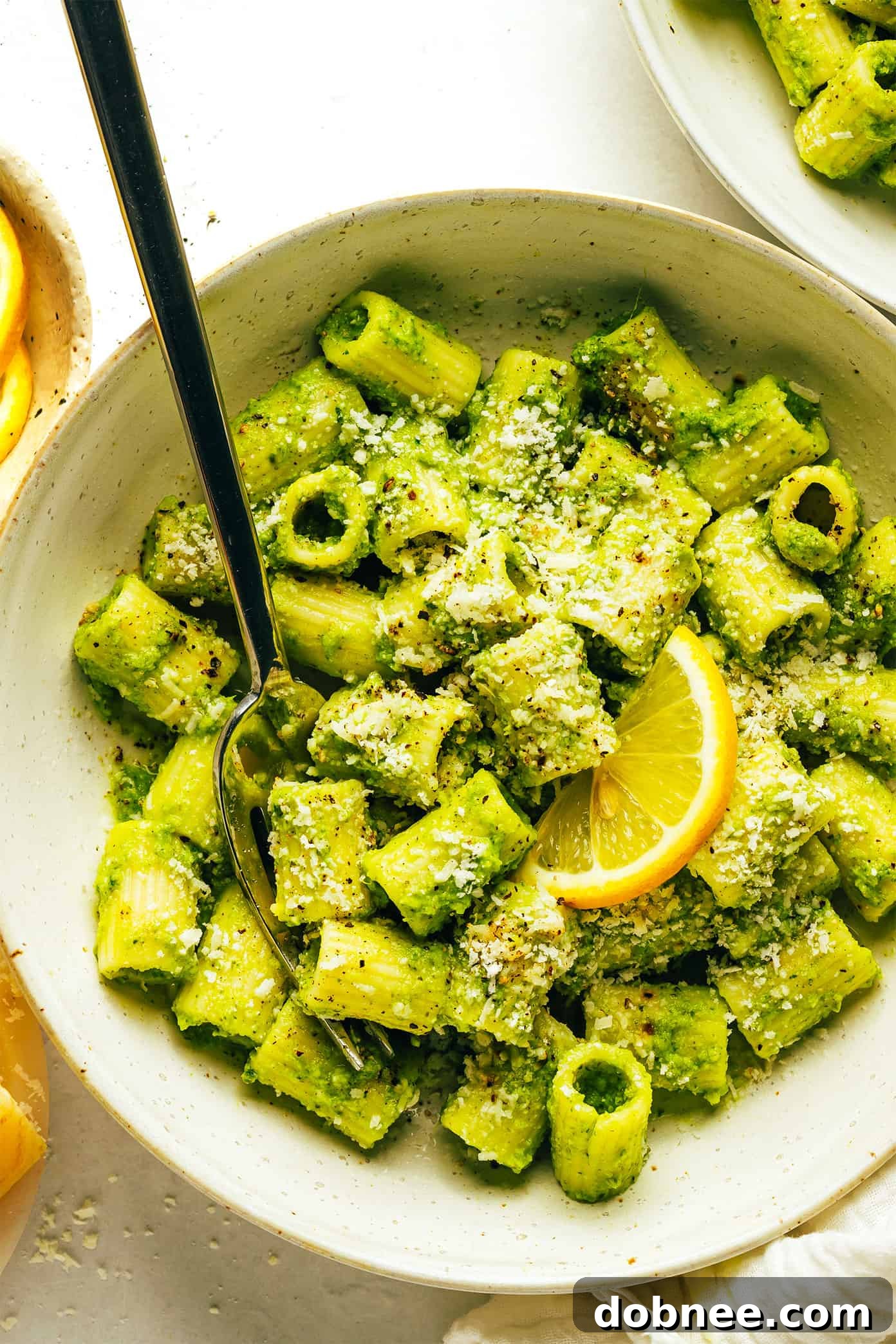 Lemony Broccoli Pesto Pasta garnished with fresh basil, lemon, and Parmesan, served in a bowl on a rustic surface.