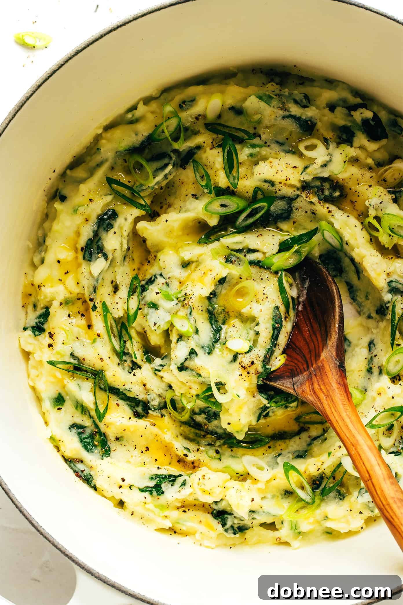 A vibrant bowl of Colcannon, Irish mashed potatoes with kale, garnished with fresh green onions.
