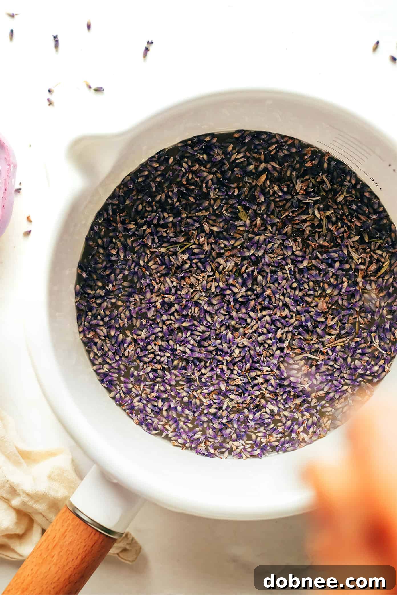 Lavender syrup being poured into a heat-safe jar after straining.